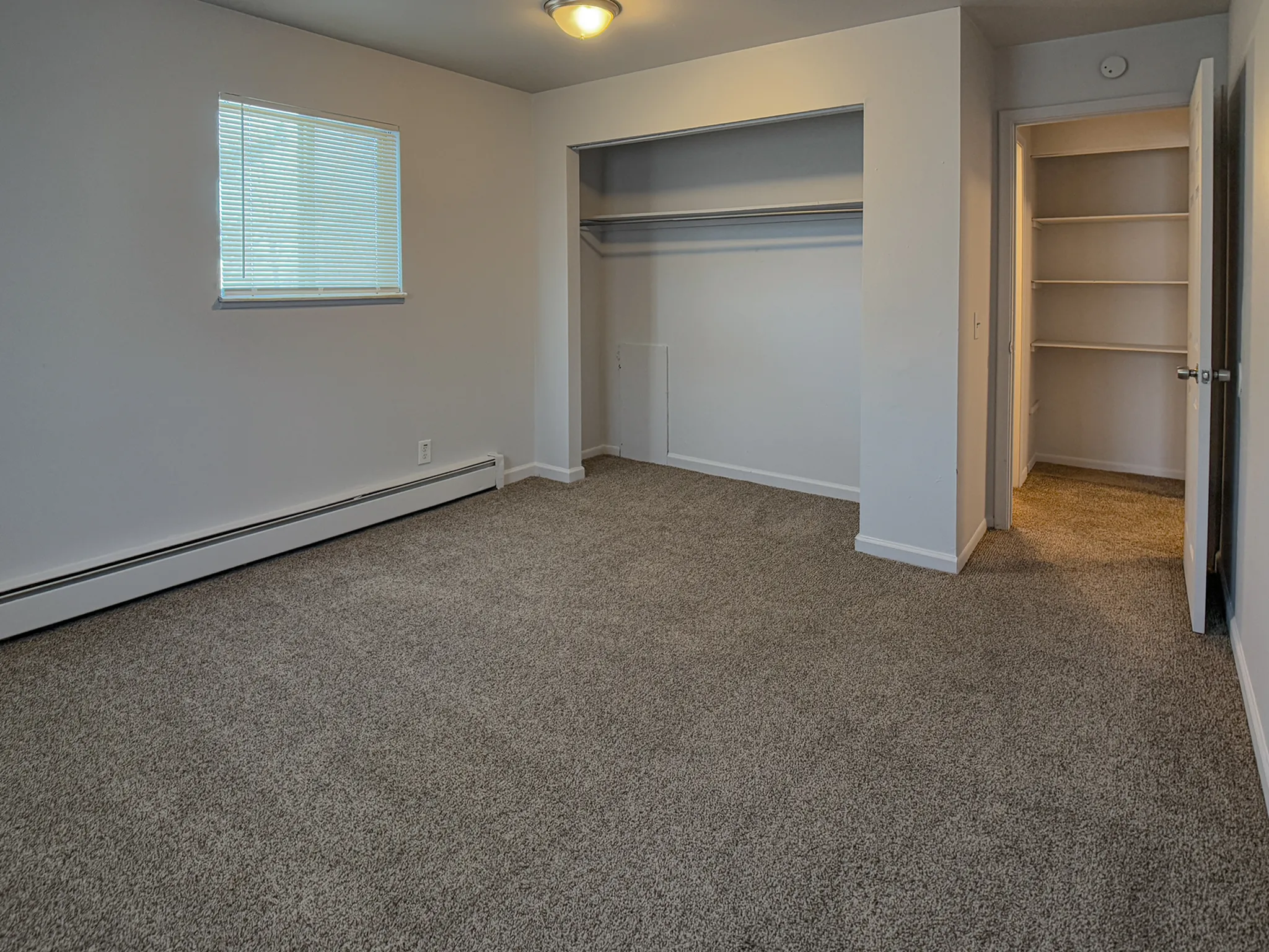 Bright and spacious bedroom featuring soft carpet flooring, large closet space, and natural light from a window, perfect for comfortable living.
