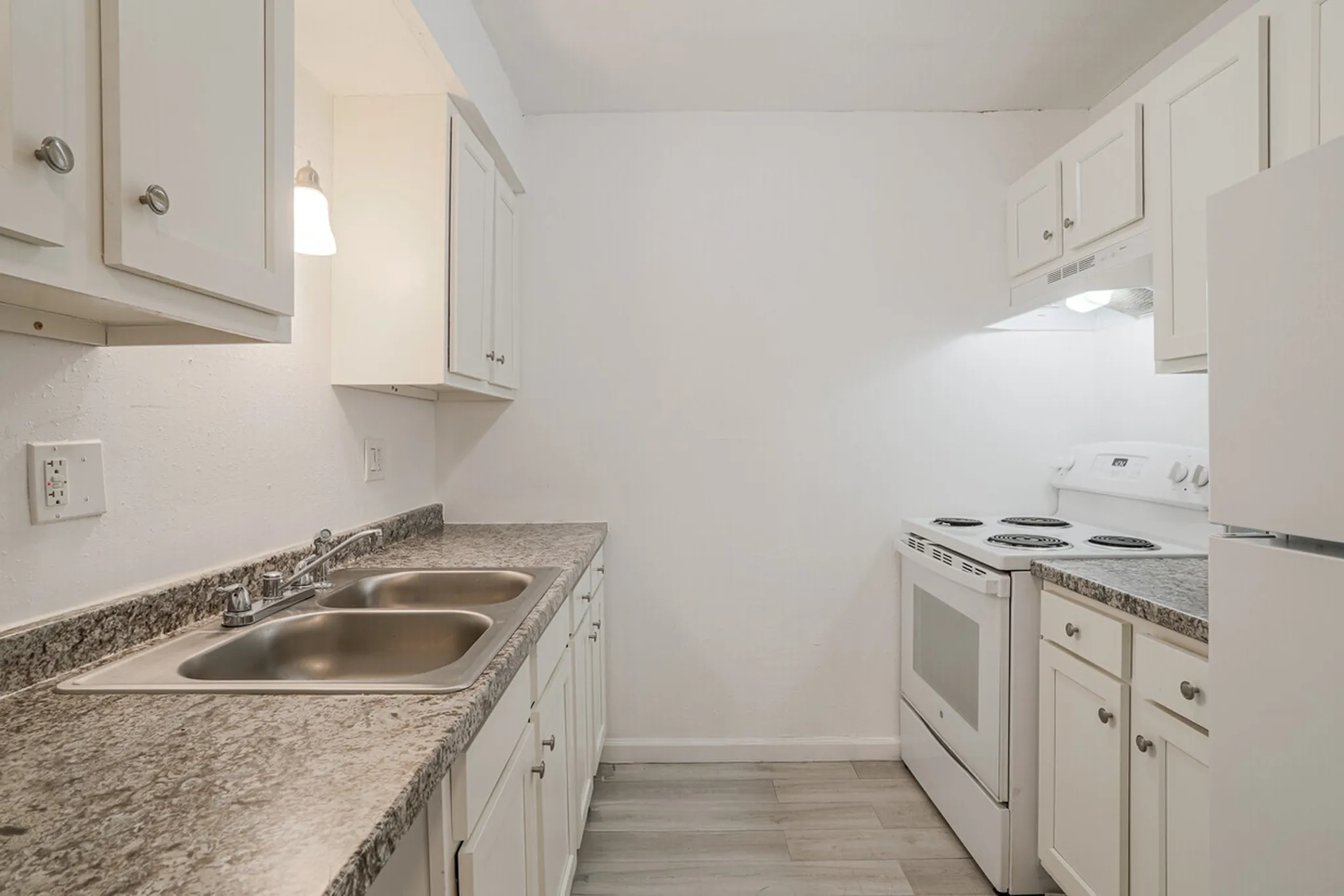 Modern kitchen with sleek granite countertops, white cabinetry, and stainless steel double sink, offering a bright and functional cooking space.