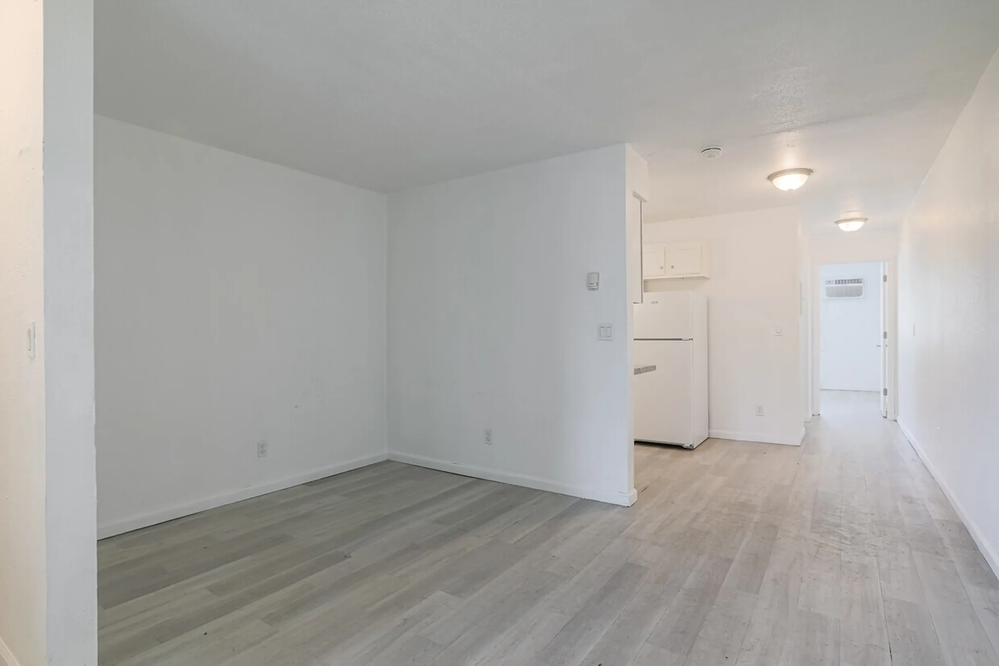 Bright, open-concept apartment space with modern light wood flooring, featuring a cozy kitchen area with crisp white cabinetry and appliances.