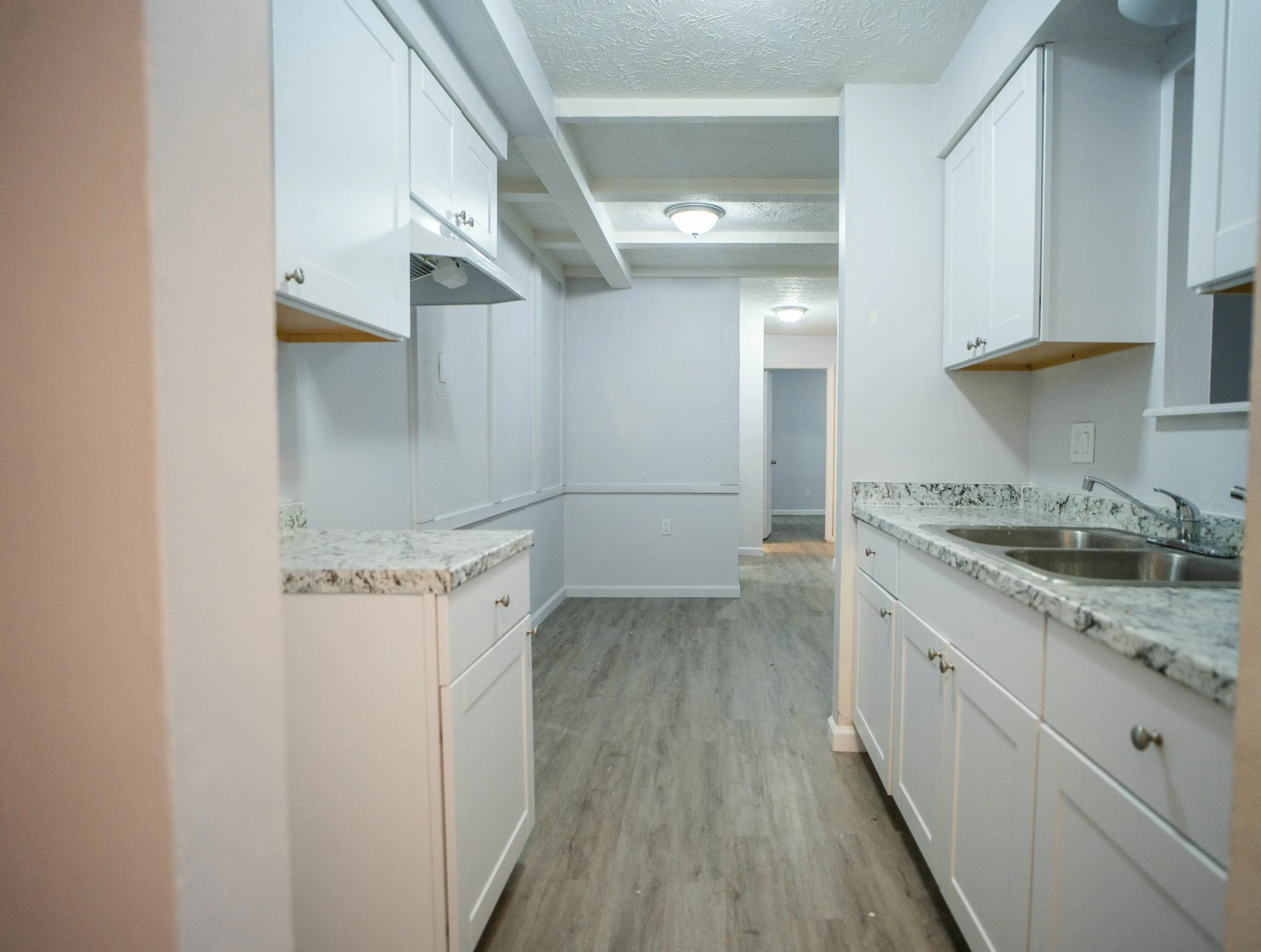 Modern galley kitchen with sleek white cabinetry, granite countertops, and durable wood-style flooring, perfect for culinary creativity.