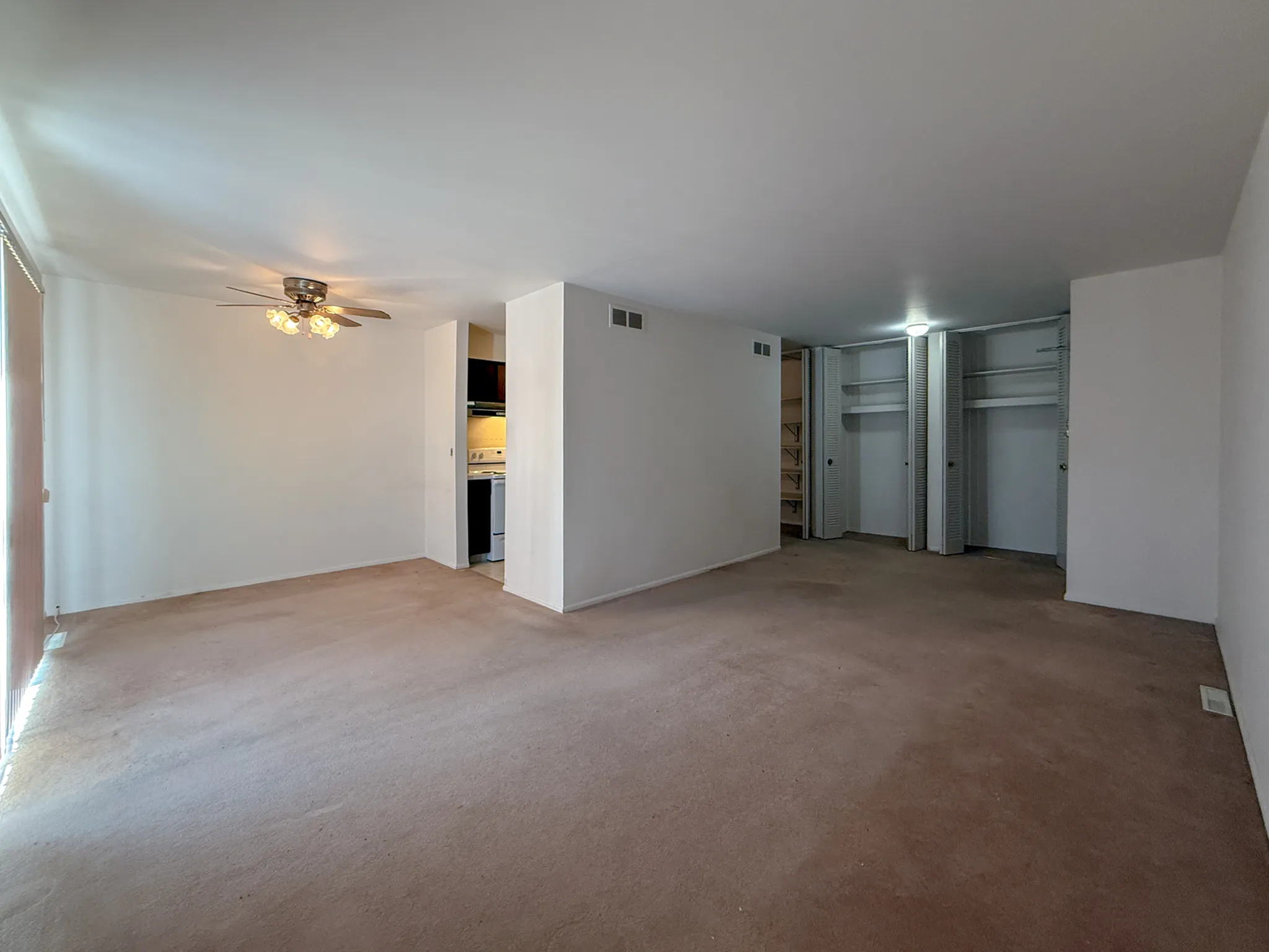 Spacious living room with plush carpet, ceiling fan, and ample natural light, leading to a cozy kitchen area.