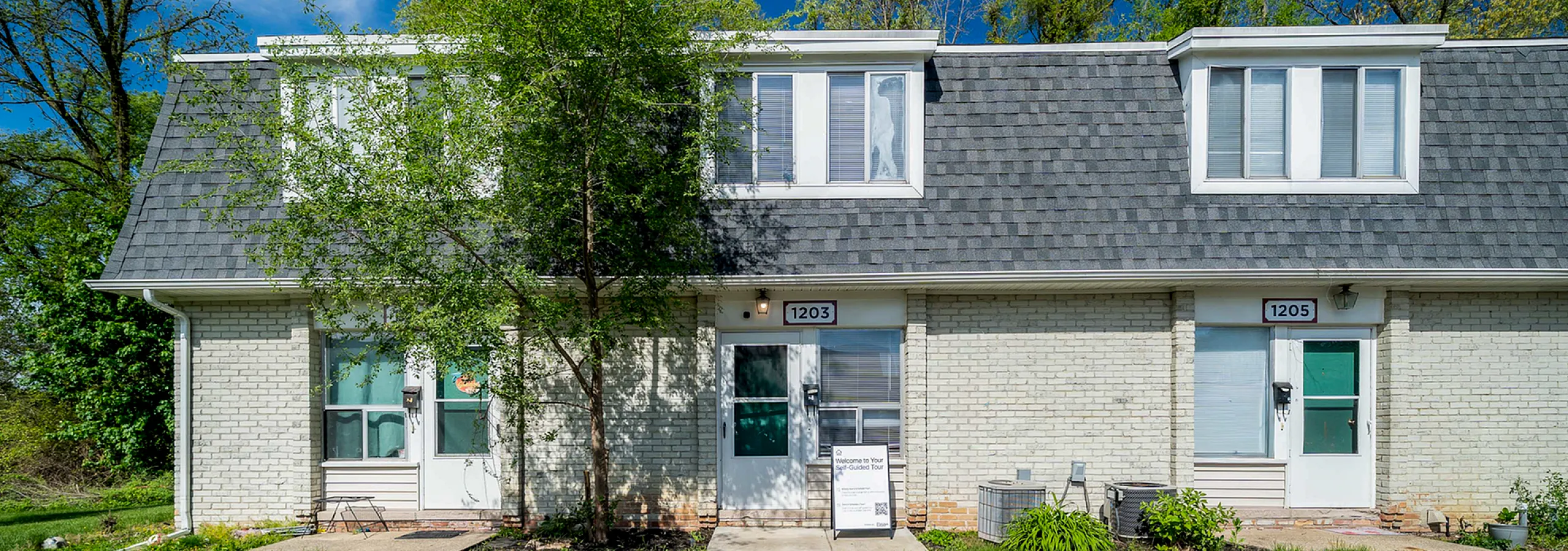 Charming townhouse with a modern exterior, featuring a grey roof, lush green lawn, and vibrant trees enhancing the curb appeal.