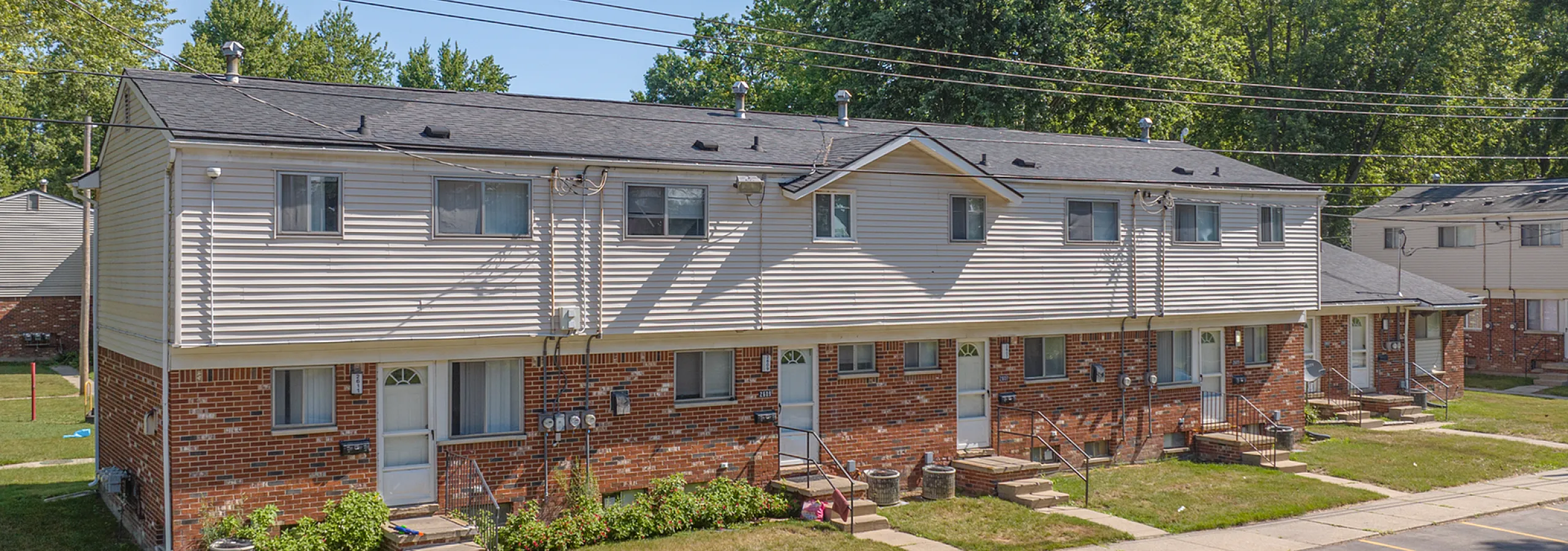 Charming multi-unit townhouse with classic brick facade, nestled in a serene residential area with lush greenery.
