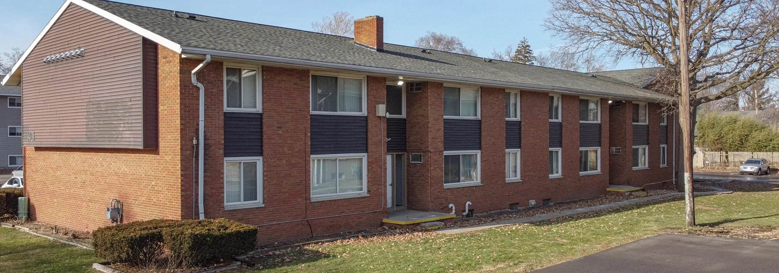 Charming two-story brick apartment building with large windows and well-maintained landscaping, set in a serene neighborhood.