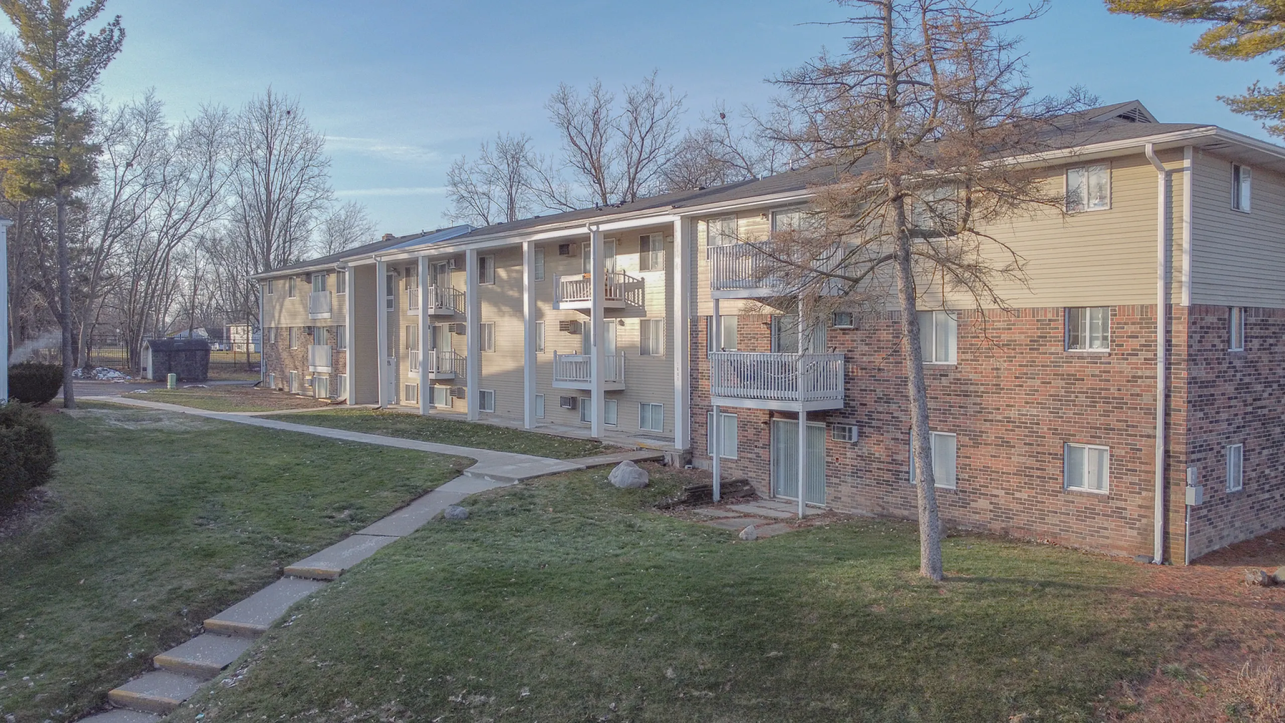 Charming brick and siding apartment complex with balconies, nestled in a serene, tree-lined setting.