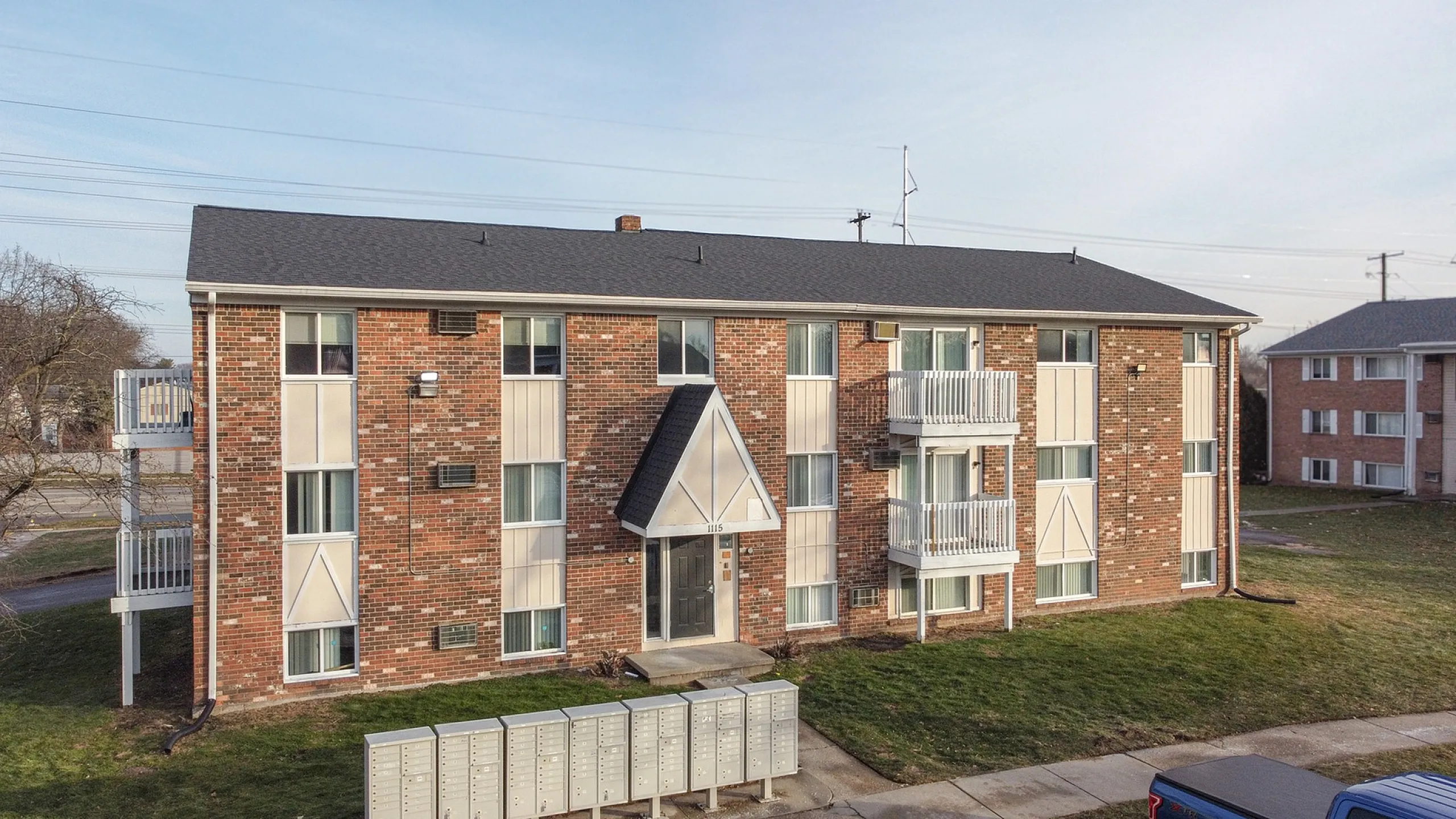 Charming brick apartment building with modern balconies, large windows, manicured lawns, and ample parking, offering a cozy community feel.