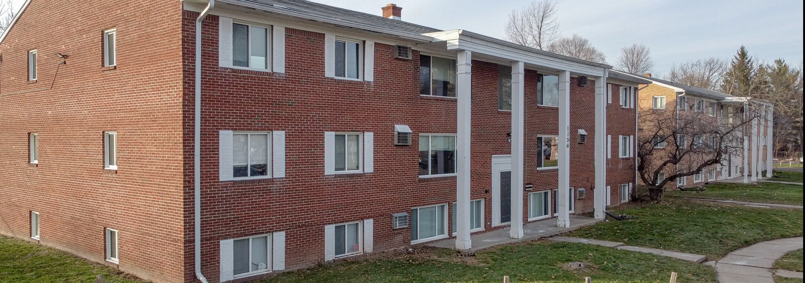 Charming red-brick apartment building with classic white columns, nestled in a serene suburban setting.