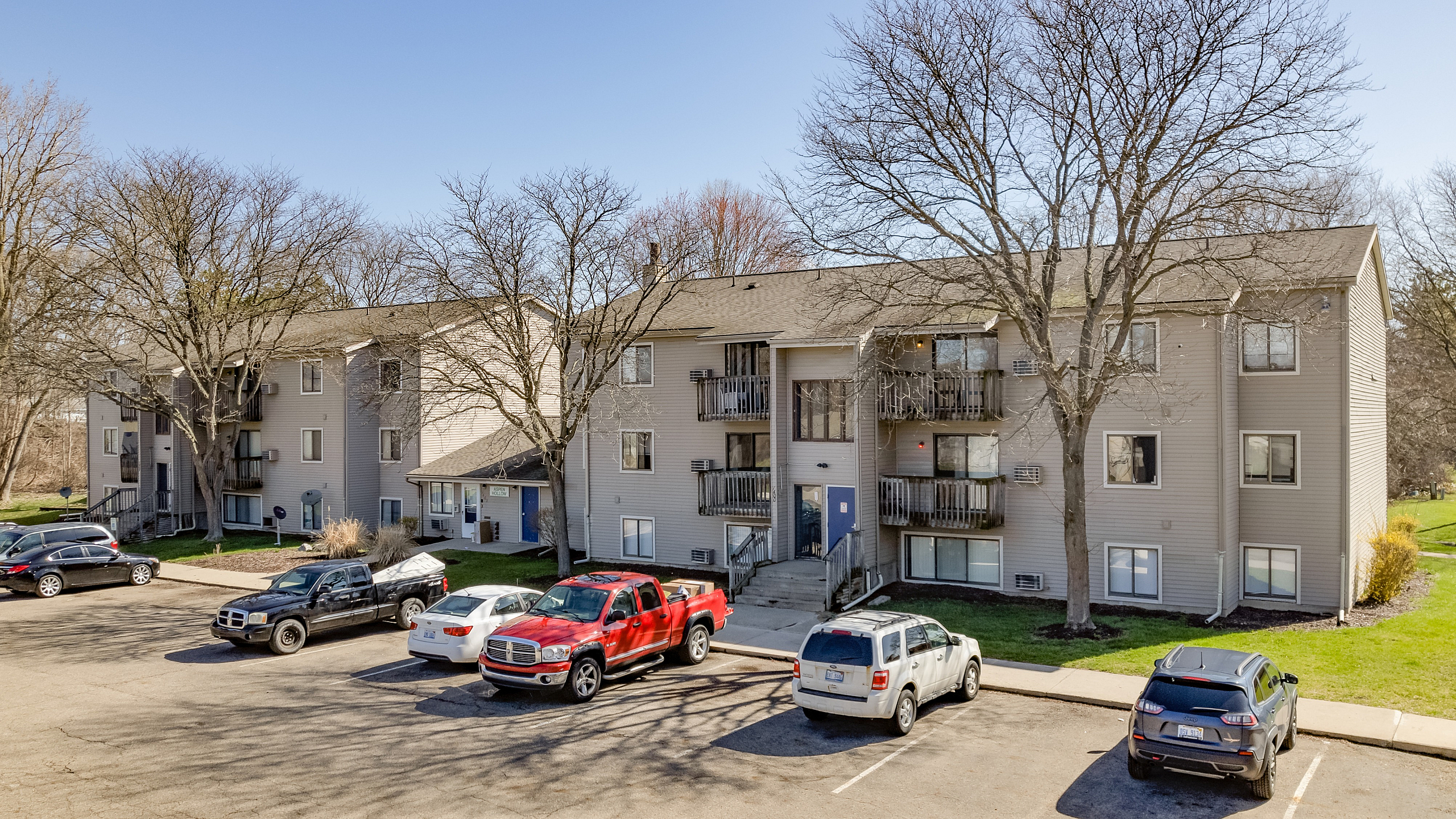 Inviting apartment building surrounded by lush greenery, featuring private balconies and ample parking space in a serene neighborhood setting.