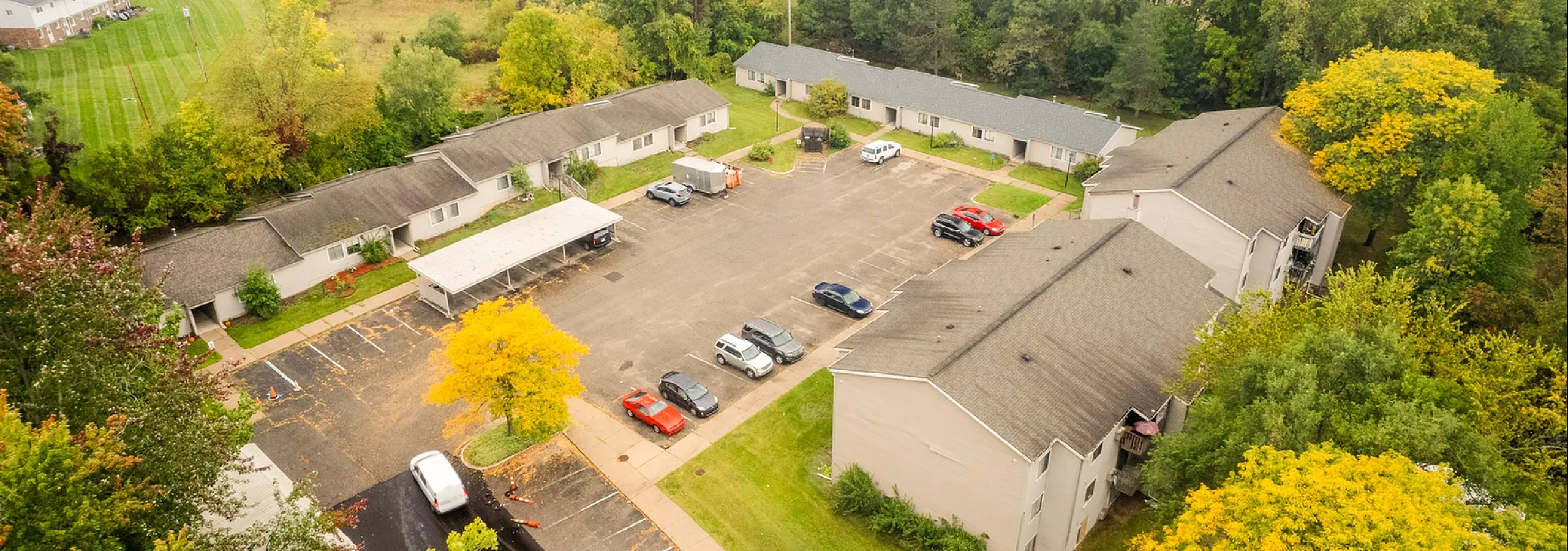 Charming aerial view showcasing a sunny apartment complex surrounded by lush greenery and a spacious parking area.