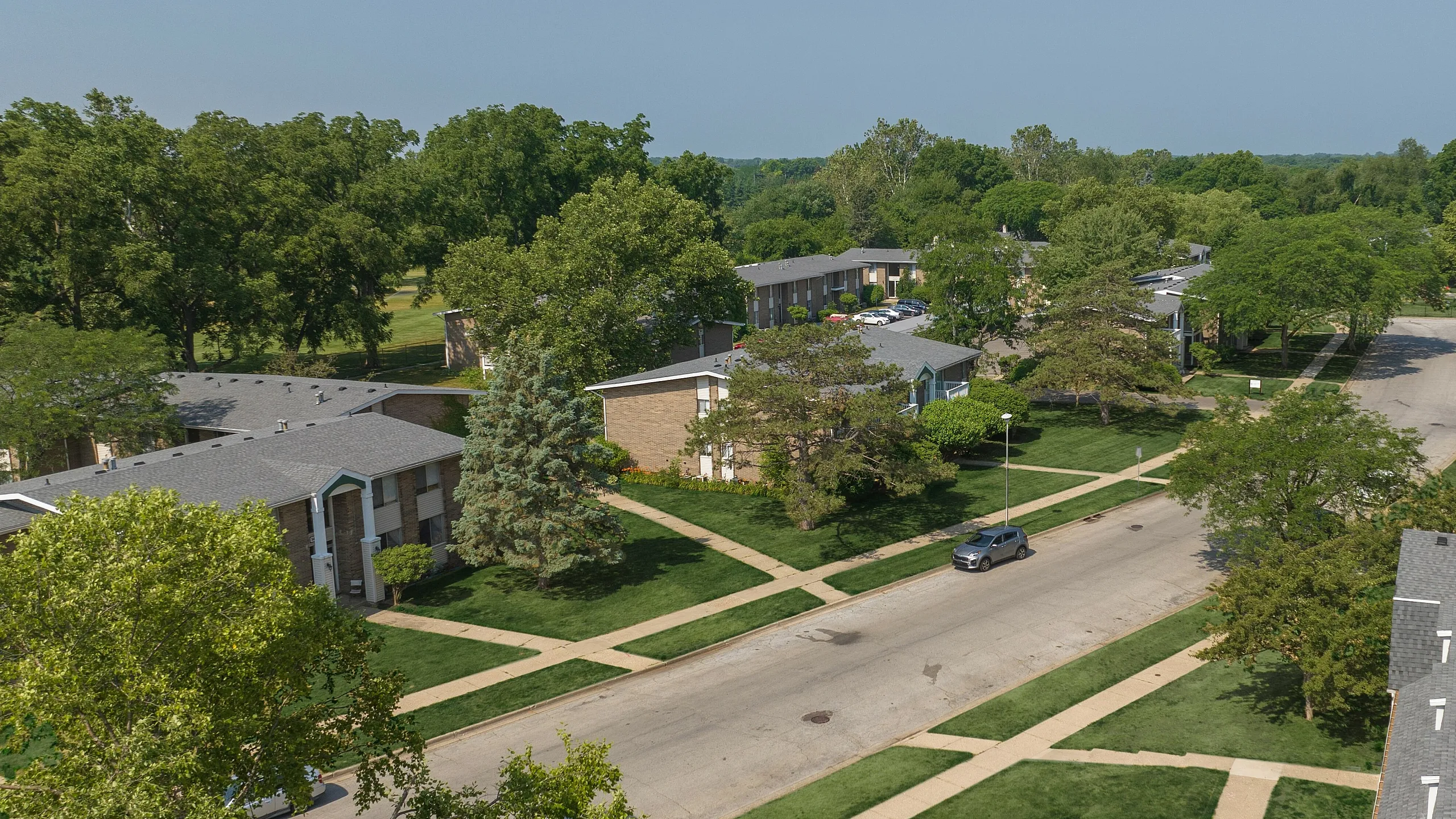 Aerial view of a charming residential neighborhood showcasing well-maintained apartment buildings surrounded by lush greenery and tree-lined streets, creating an inviting and serene environment.