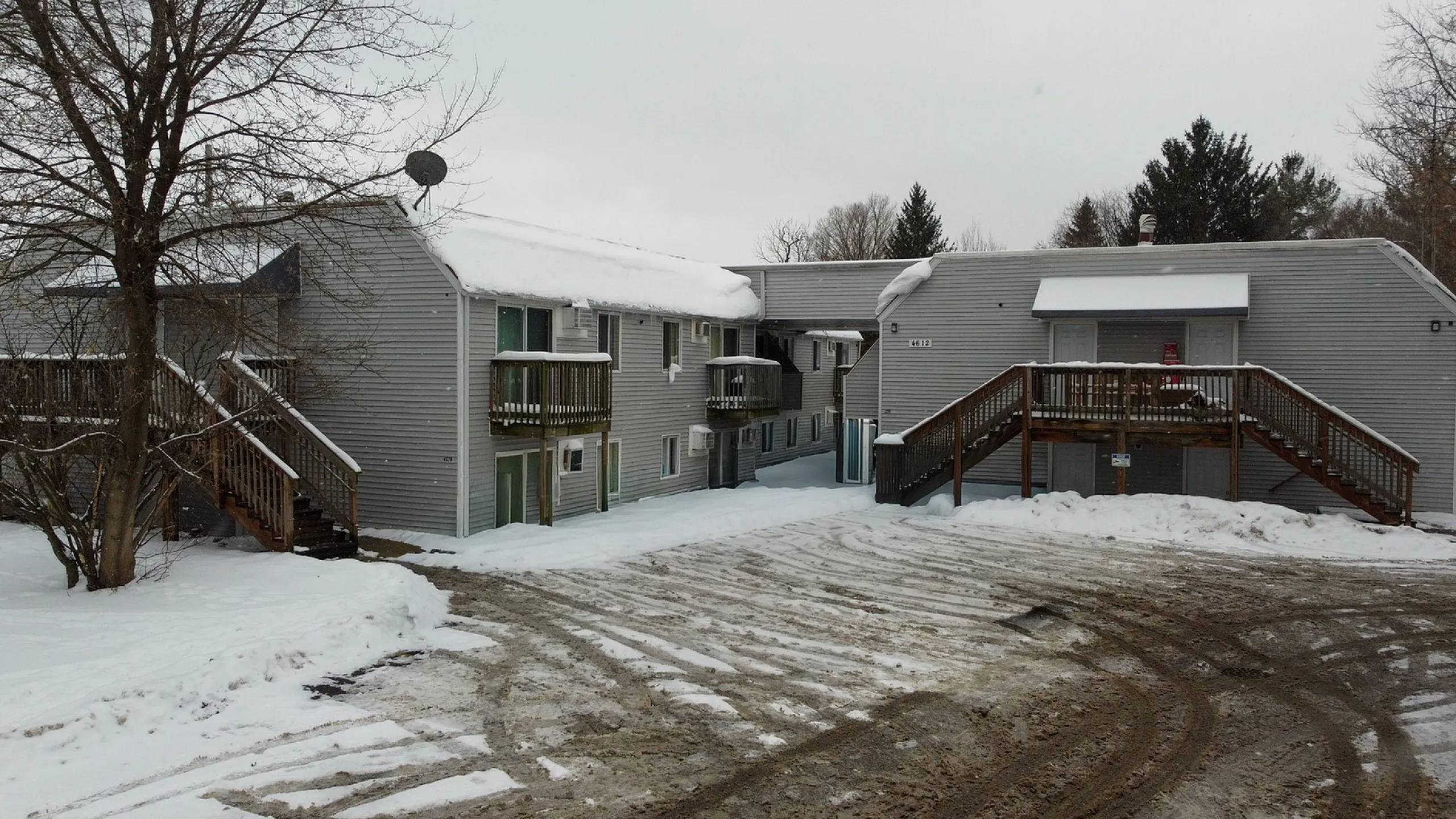 Charming snow-covered apartment complex with wood-panel exterior, featuring dual-level access and ample balcony views.