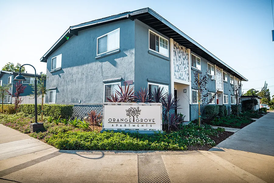 Charming Orange Grove Apartments with modern design, surrounded by lush landscaping and clear blue skies.