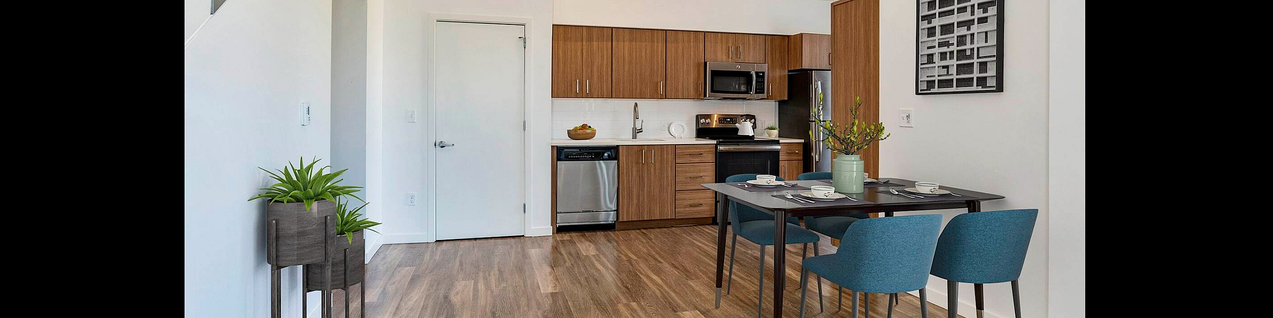 Modern apartment interior showcasing an open-concept kitchen with sleek wooden cabinetry, a stylish dining area with blue chairs, and a cozy living space adorned with contemporary art and lush greenery.