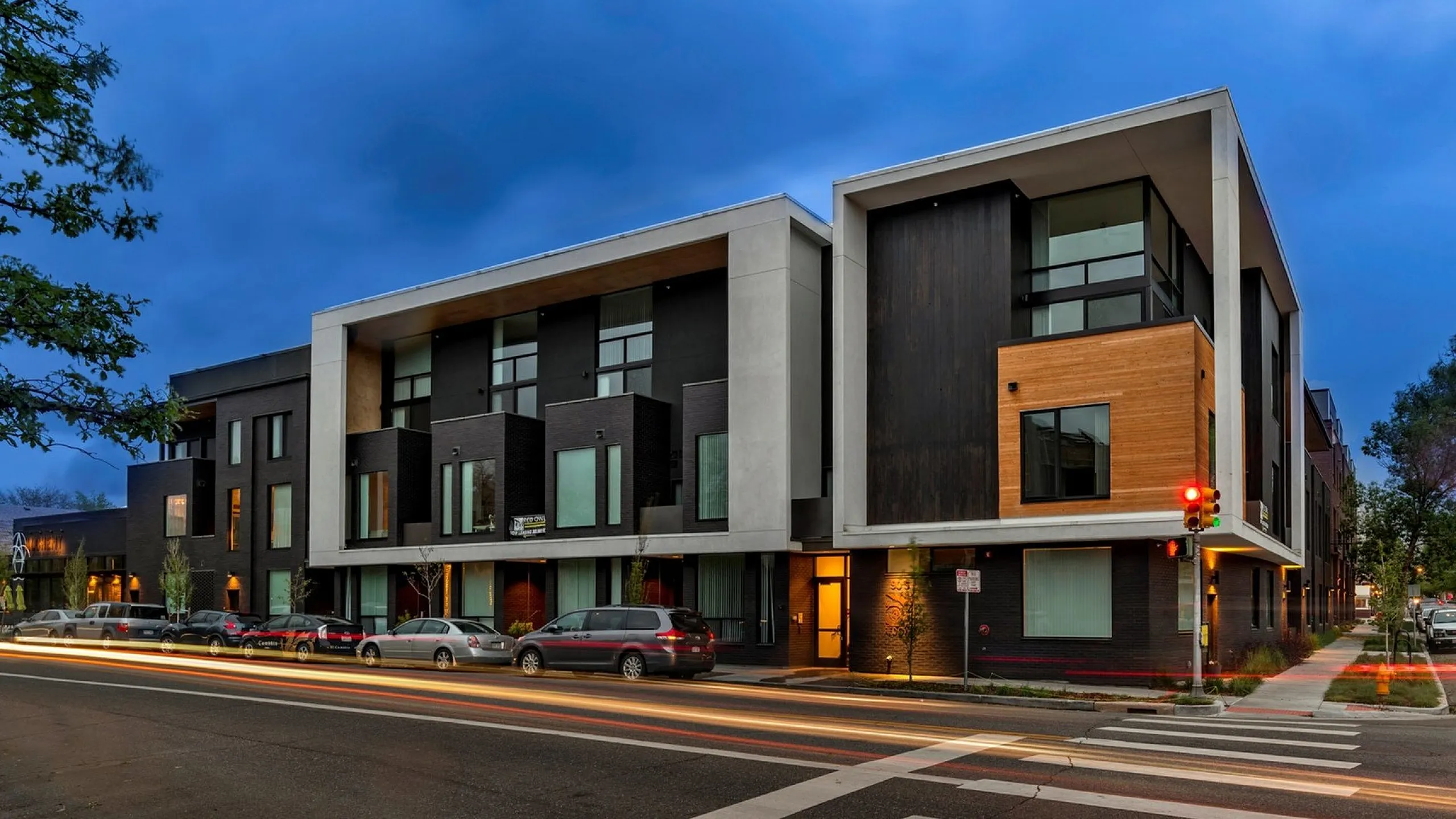 Contemporary urban apartment building with modern architectural design, featuring sleek lines and mixed materials, set against an evening sky.