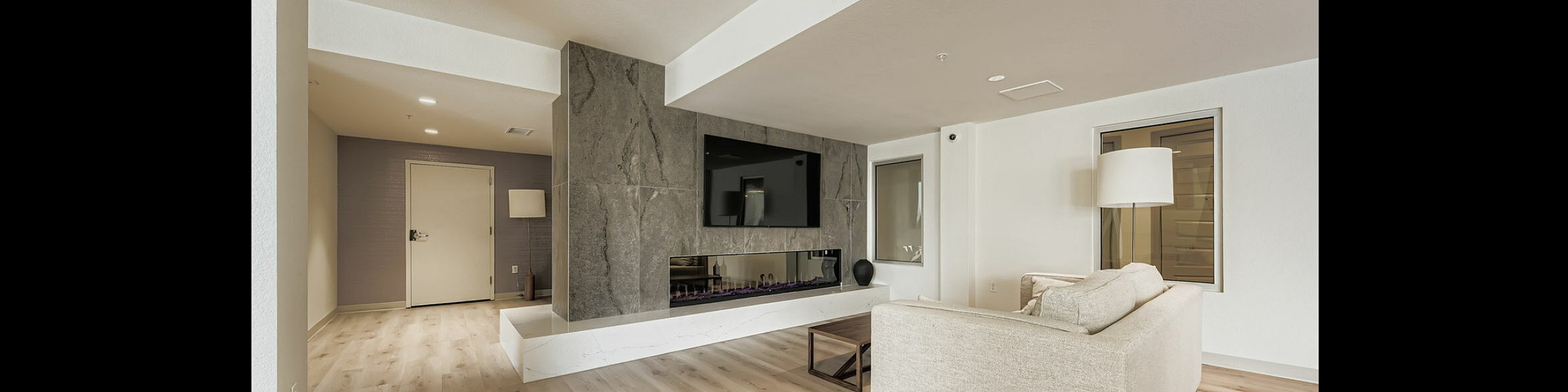 Modern club room featuring a chic stone fireplace, sleek wooden flooring, large flat-screen TV, and elegant beige sofa, offering a cozy and stylish atmosphere.