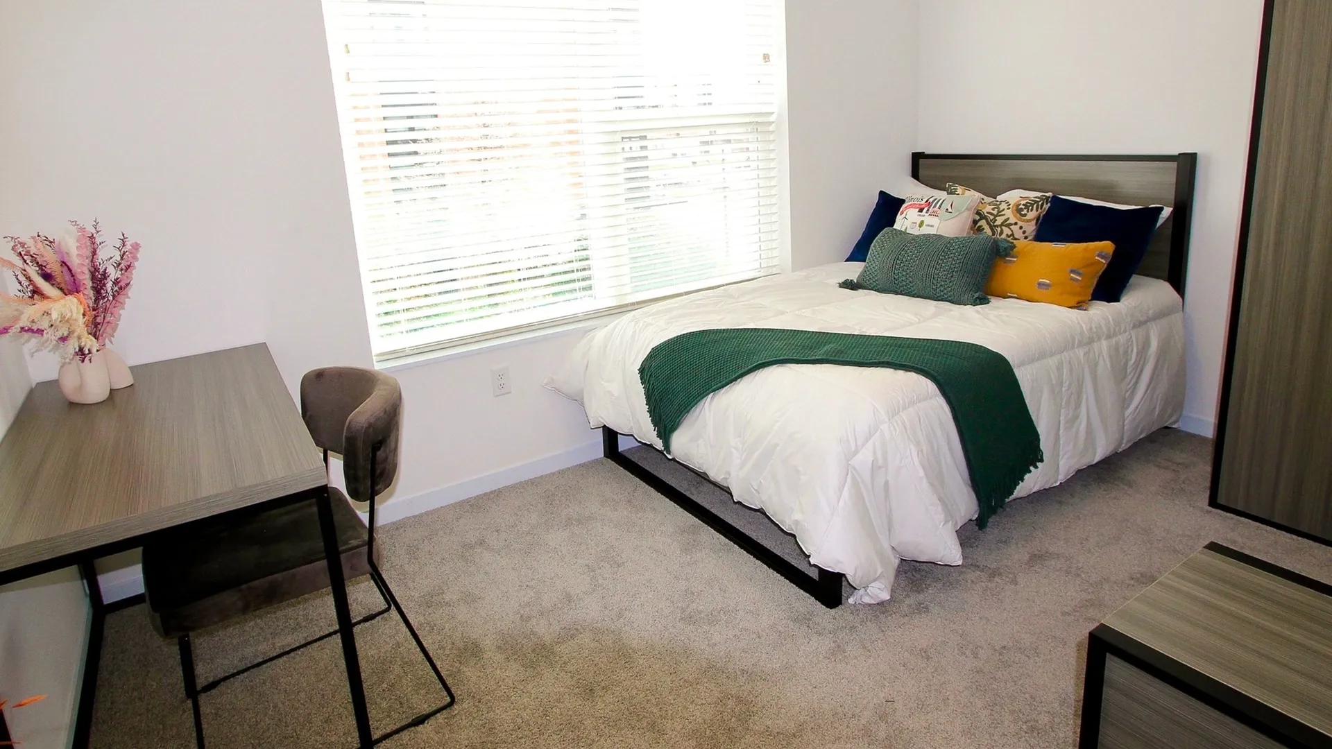 Accommodating bedroom with night stand next to a bed, study area desk, and storage unit next to window.