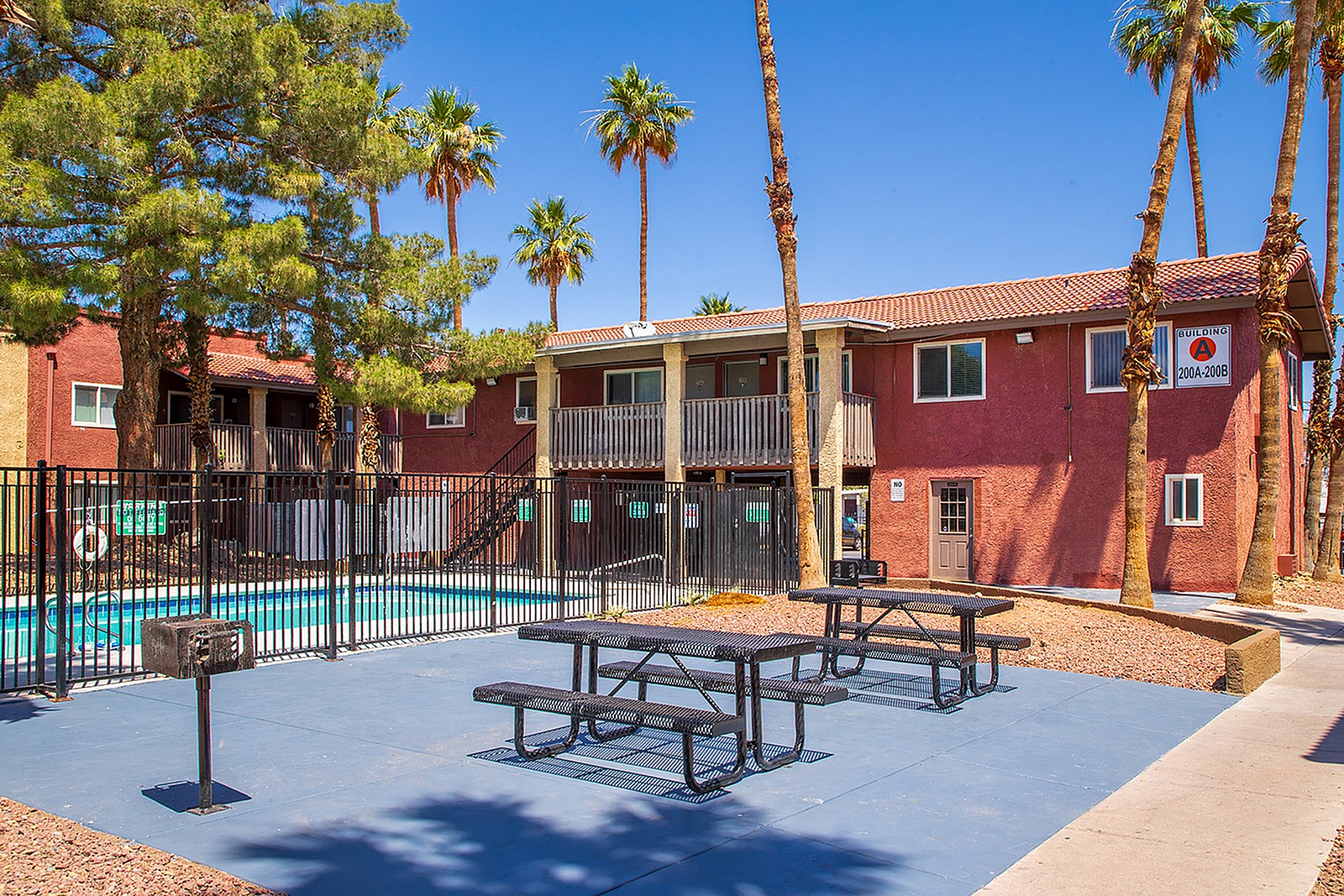 Charming apartment complex with a beautiful pool area and outdoor seating, surrounded by lush palm trees and vibrant landscaping.