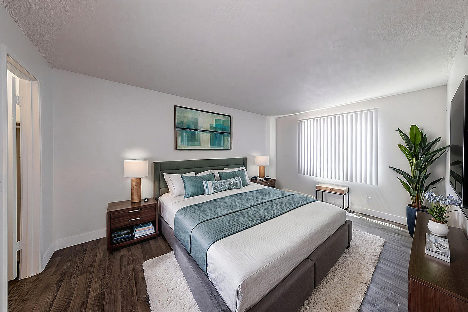 Elegant bedroom with a plush king-sized bed, modern decor, and abundant natural light from vertical blinds.