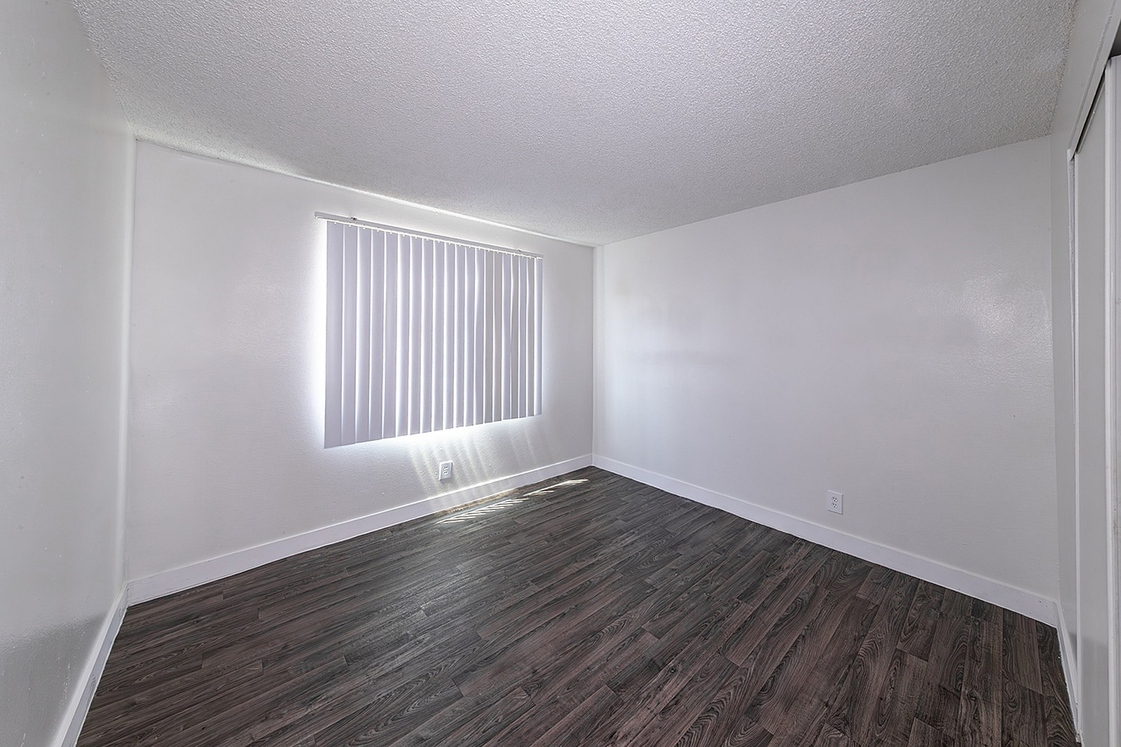 Bright and airy room with modern dark wood flooring and vertical blinds, perfect for creating a cozy and inviting living space.