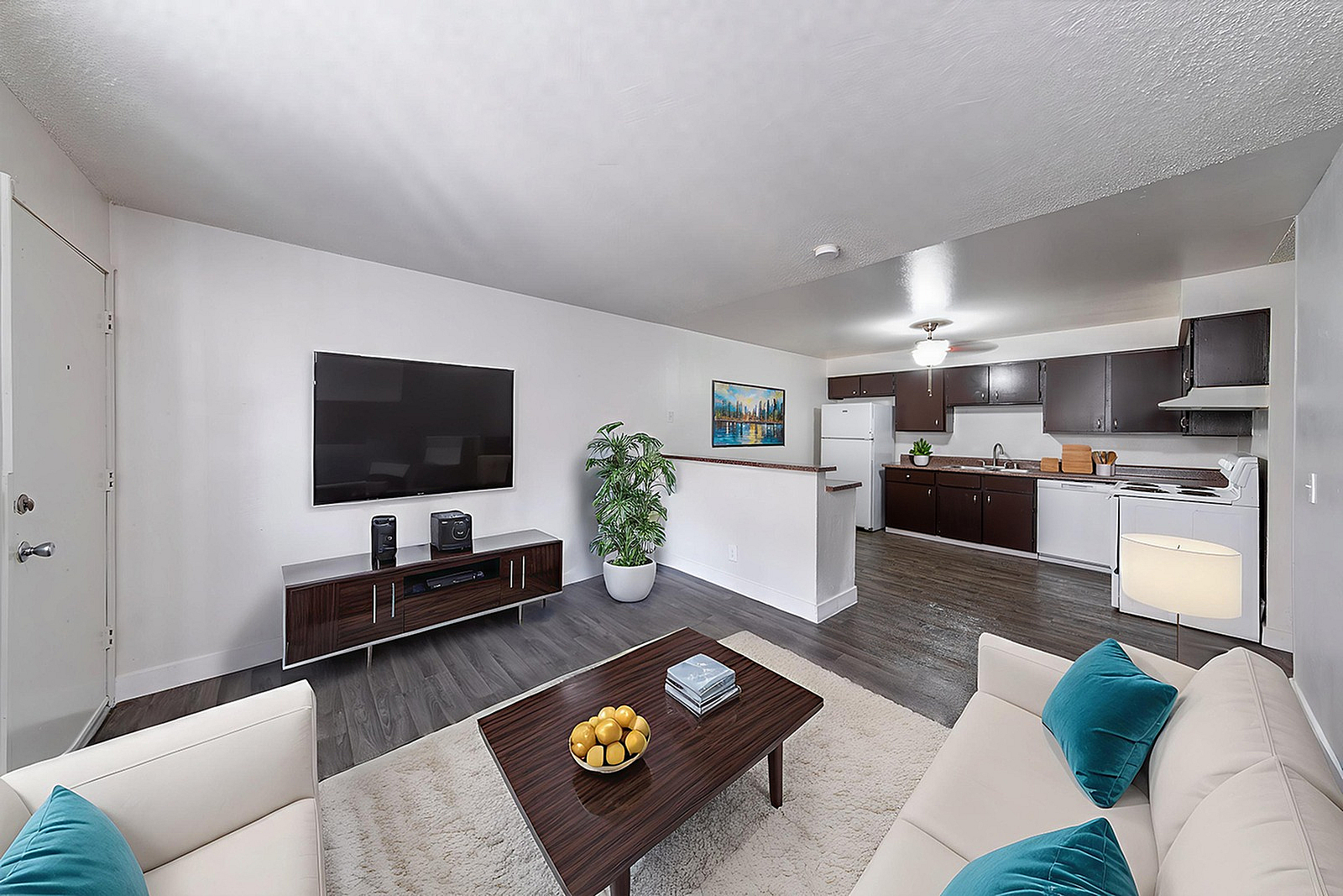 Modern open-concept living room and kitchen with sleek wood flooring, stylish dark cabinetry, and comfortable seating area.