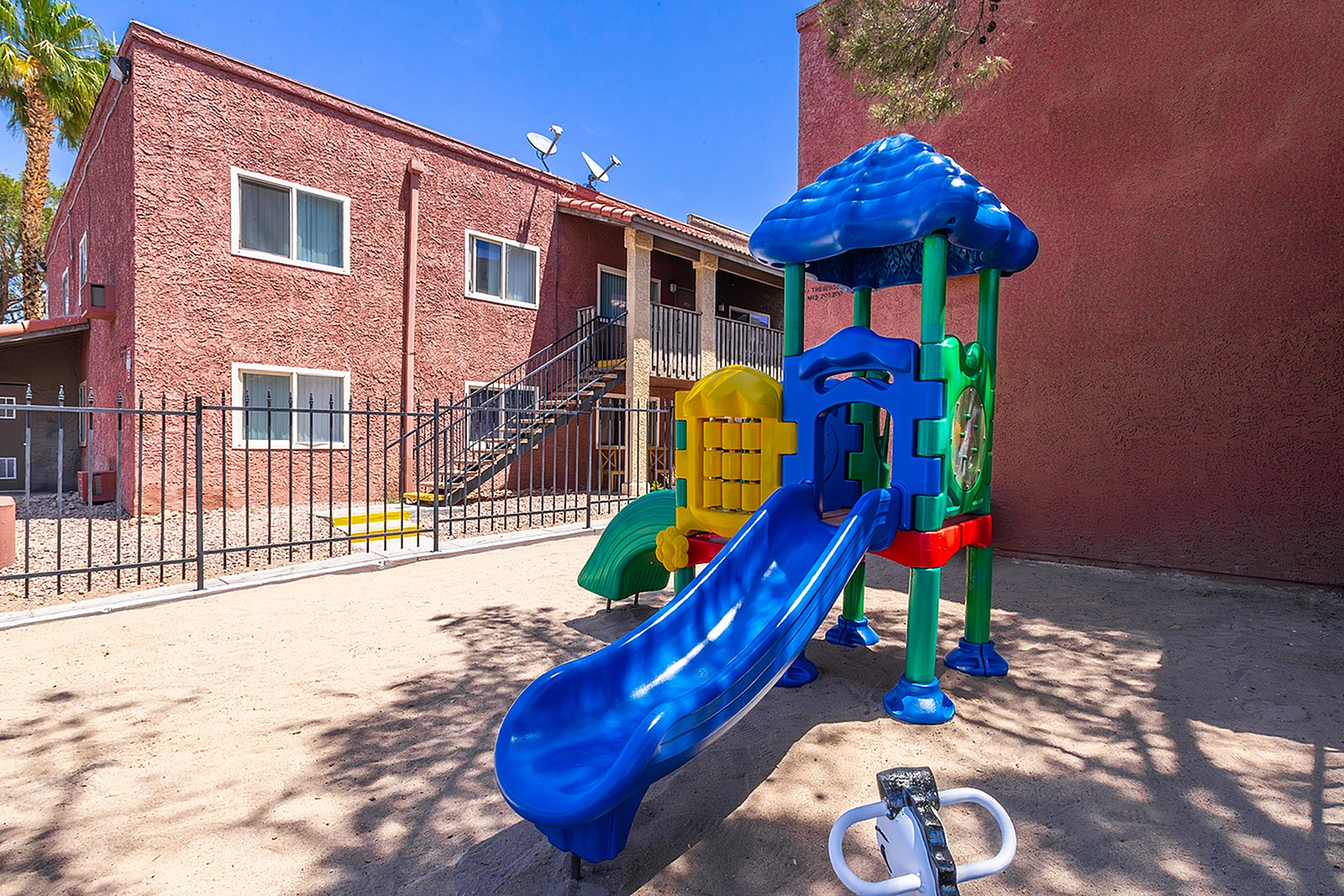 Charming apartment exterior with a vibrant children's playground featuring a colorful slide and secure fencing, perfect for families.