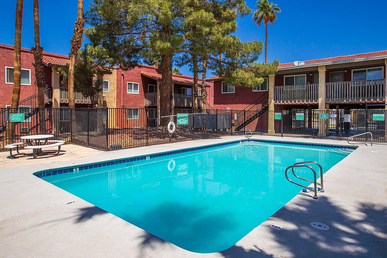 Vibrant apartment complex featuring a sparkling swimming pool surrounded by lush palm trees, perfect for relaxation and leisure.