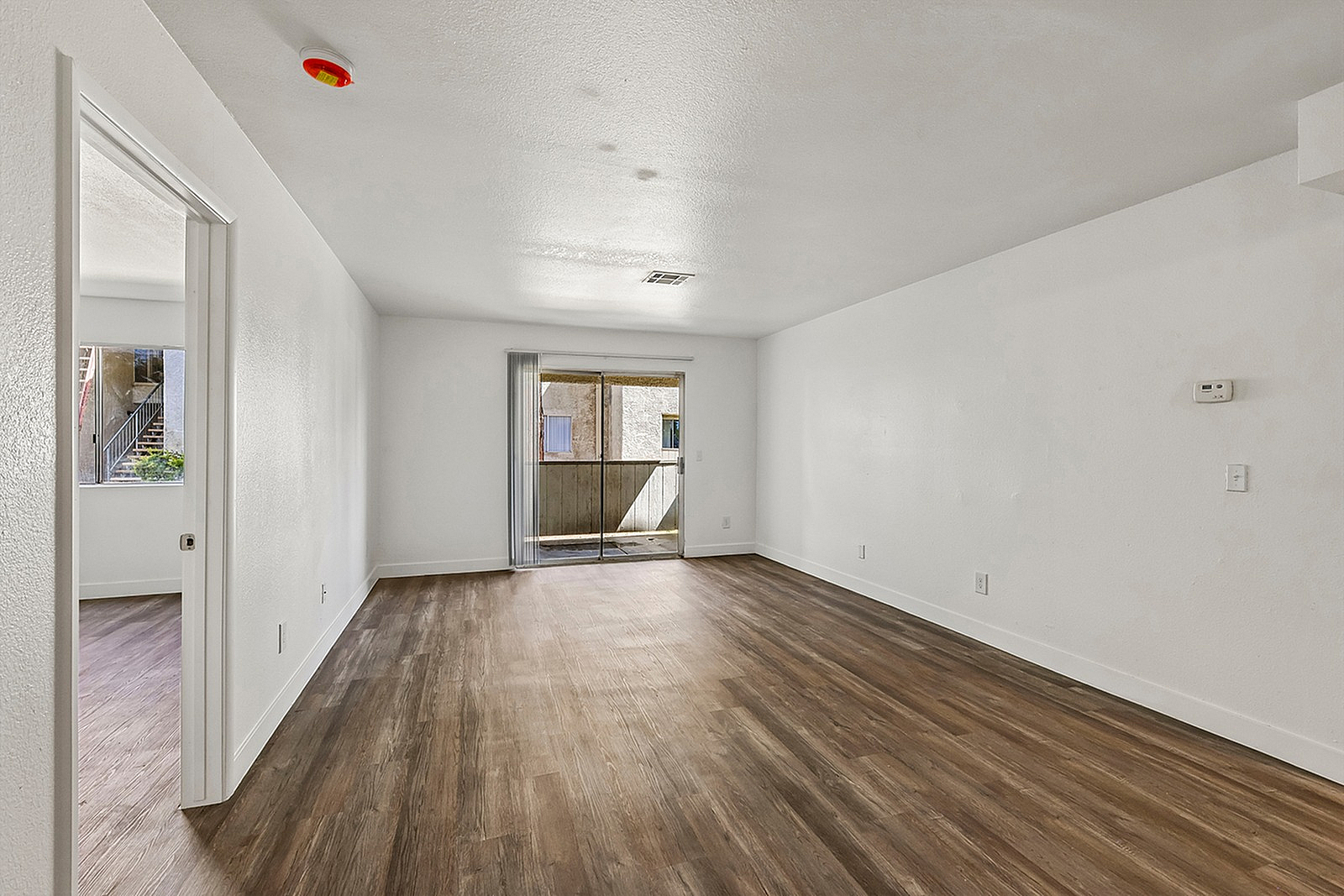 Bright and spacious living room with warm wood flooring, leading to a cozy outdoor patio through sliding glass doors.