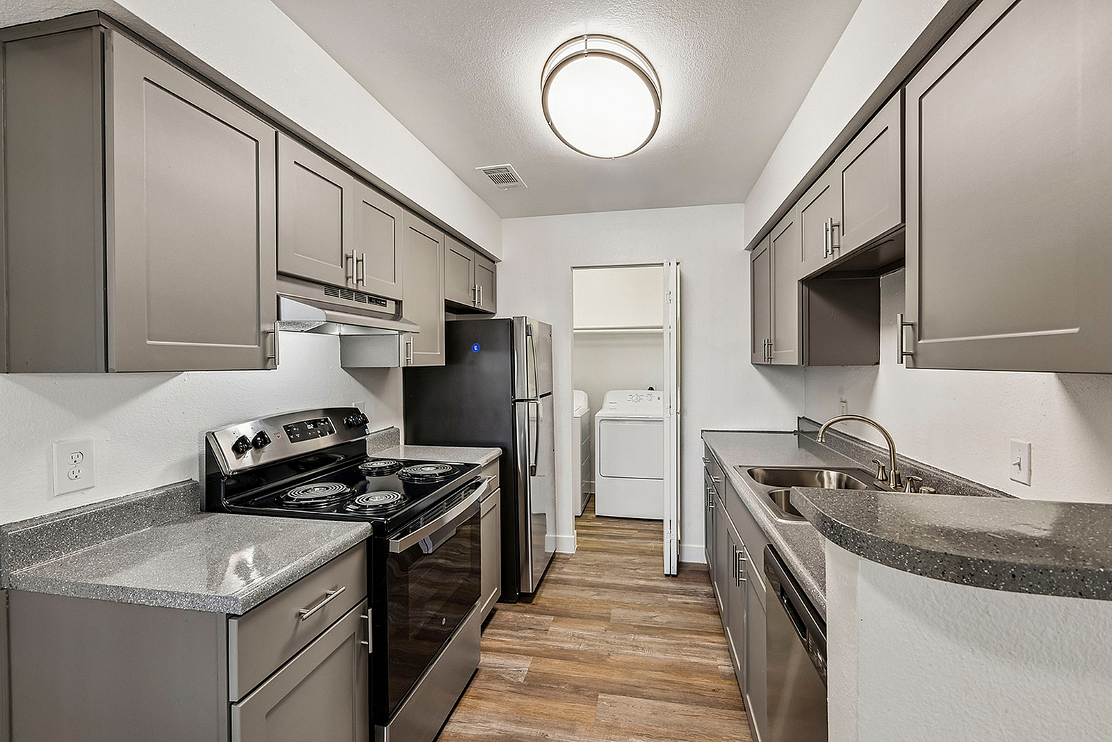 Modern kitchen with sleek gray cabinetry, stainless steel appliances, and hardwood flooring, leading to an in-unit laundry area.