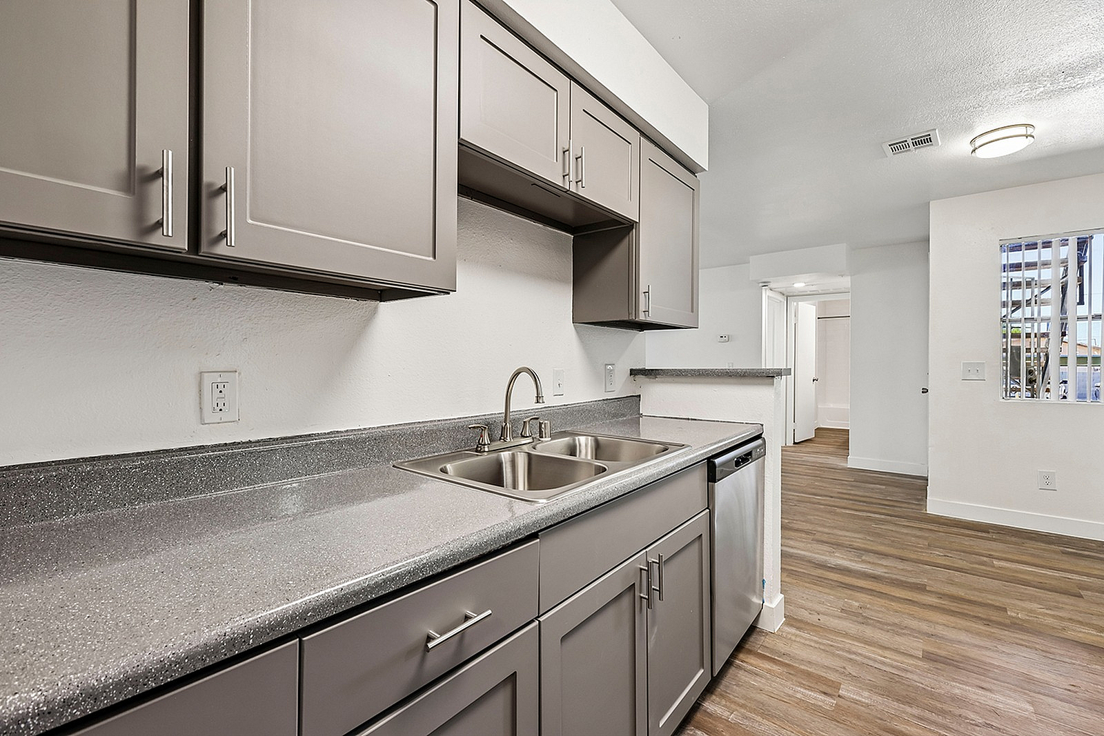 Contemporary kitchen featuring sleek grey cabinetry, double stainless steel sink, and modern appliances, complemented by elegant wood flooring and open layout.