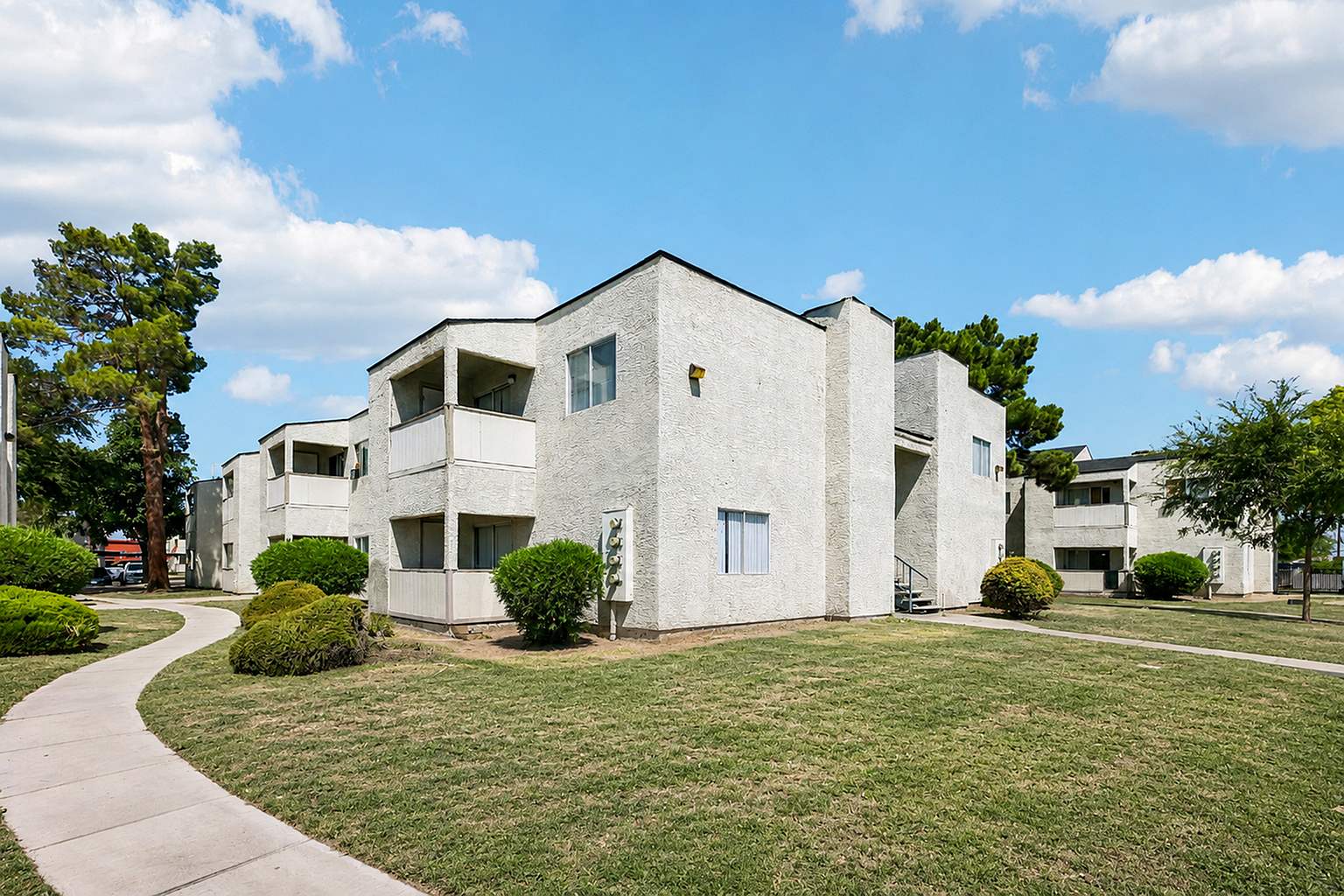 Bright and inviting apartment community with modern architecture, lush green lawns, and scenic walkways under a clear blue sky.
