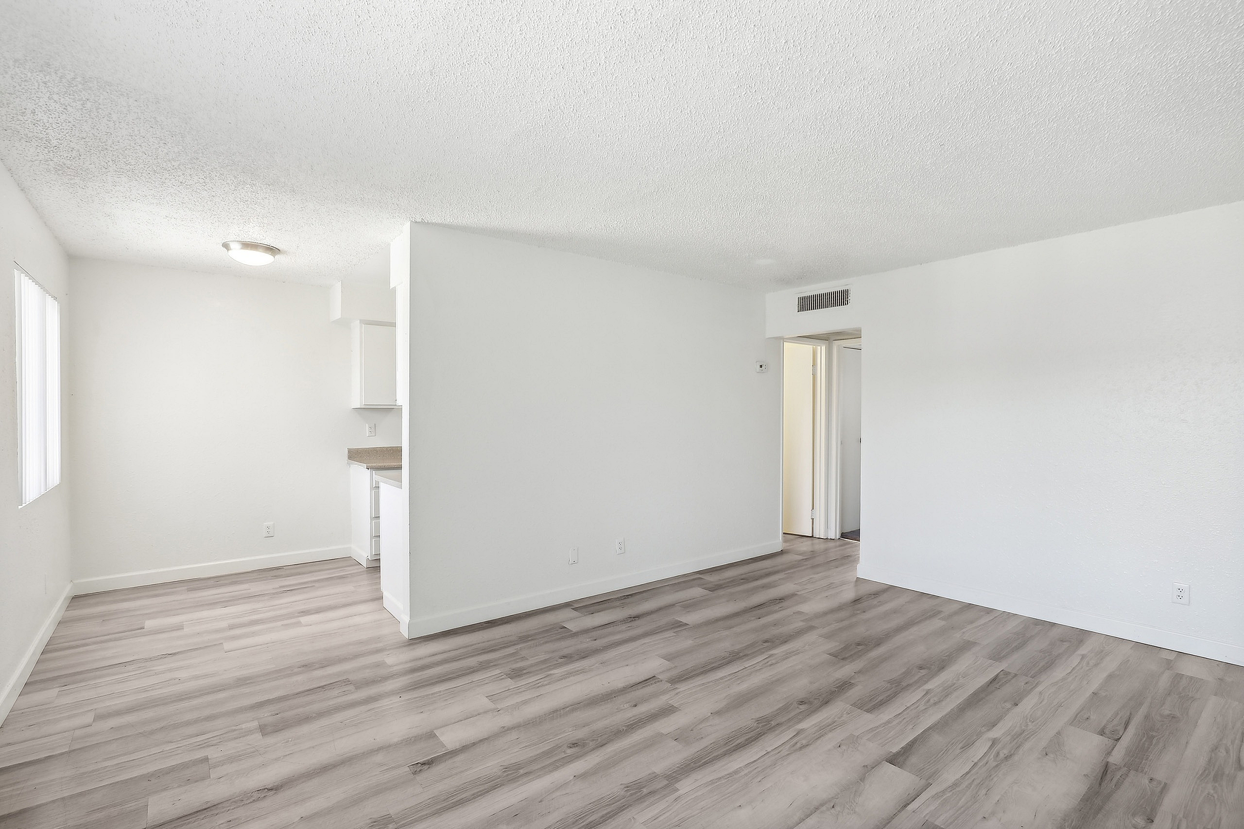 Bright and airy open living space with modern hardwood floors, inviting natural light through large windows, and a glimpse of the sleek kitchen area.