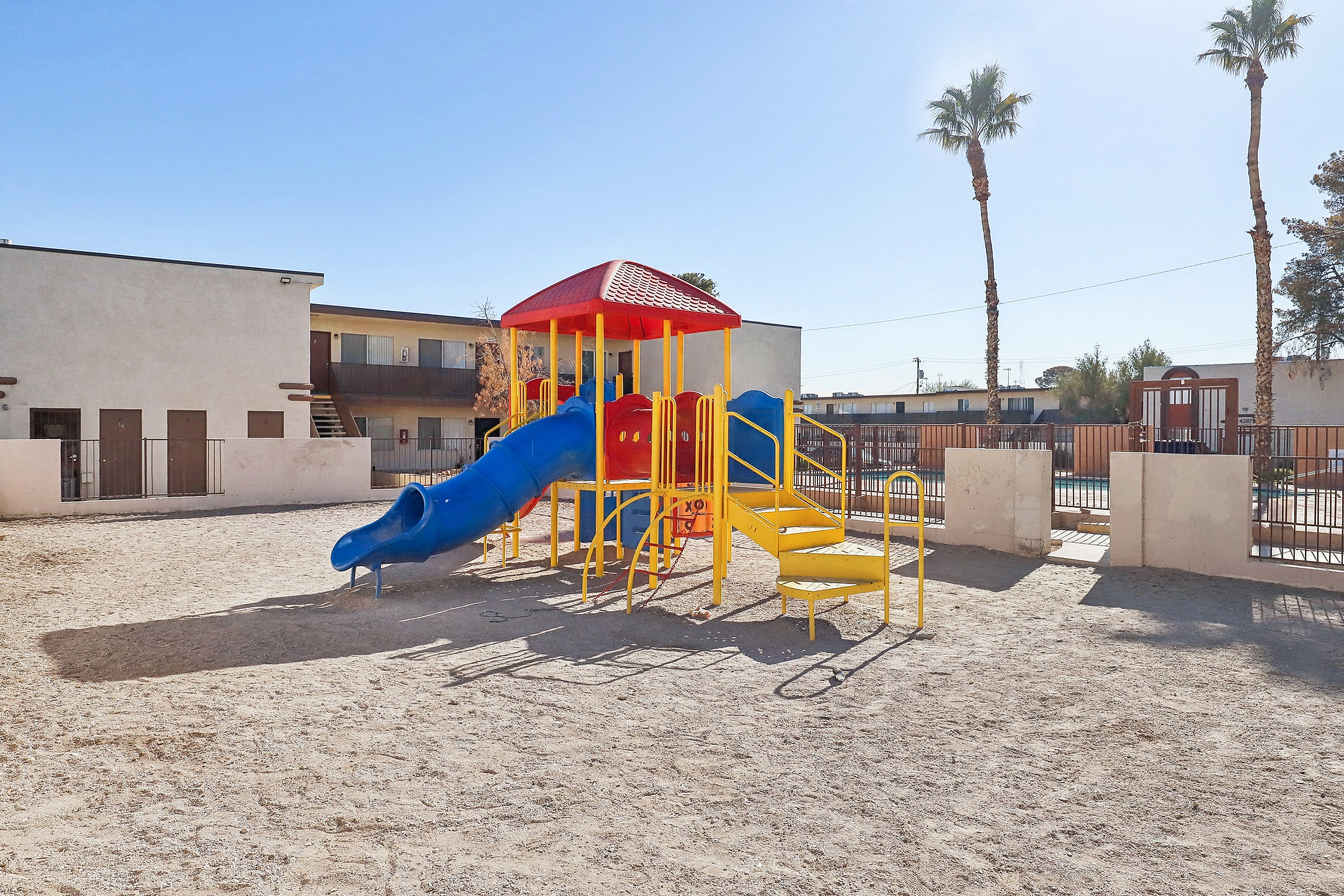 Inviting playground with a colorful slide and climbing structure set against a backdrop of modern apartments and swaying palm trees.