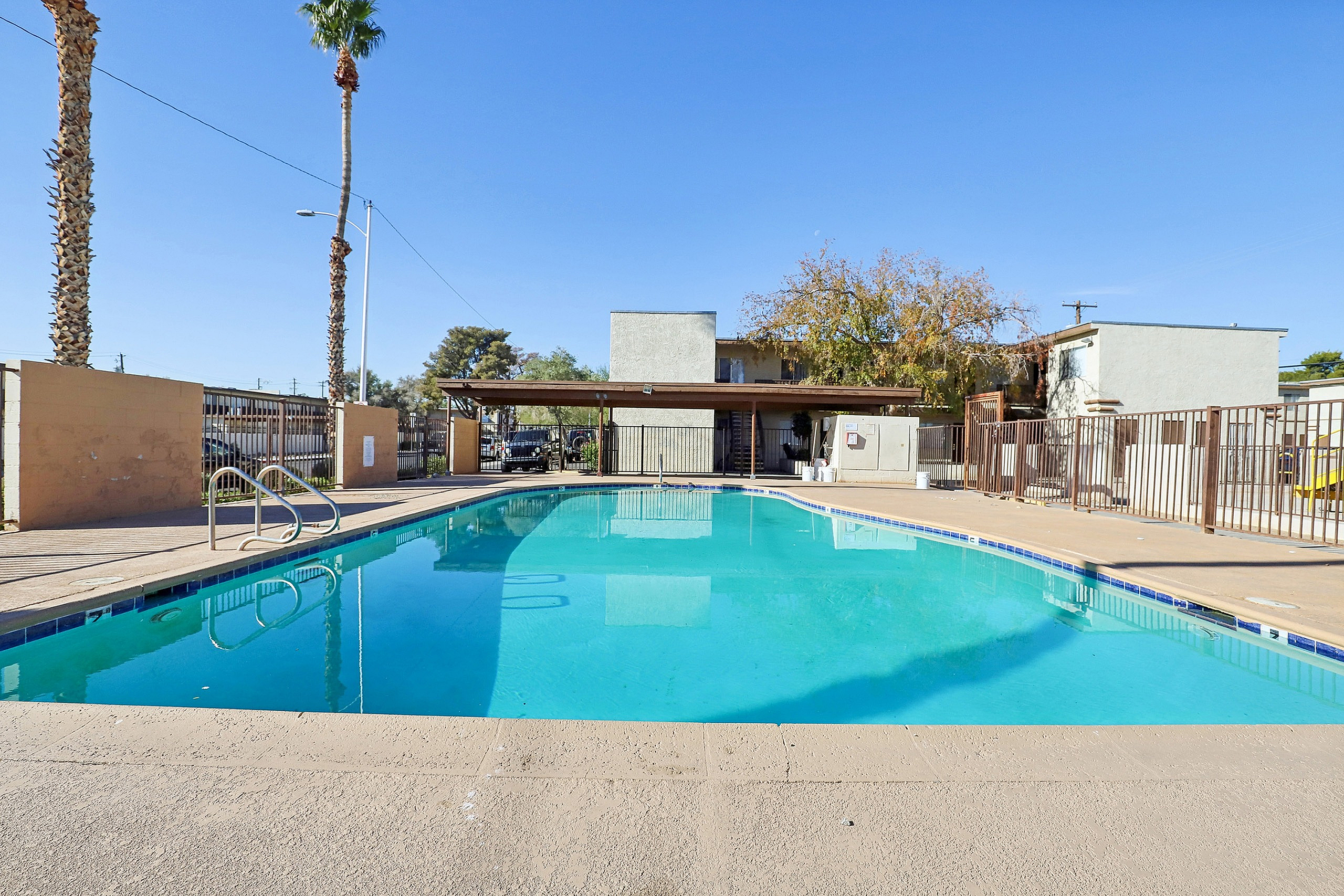 Inviting outdoor pool area with clear blue water, surrounded by secure fencing and palm trees, perfect for relaxation and leisure.