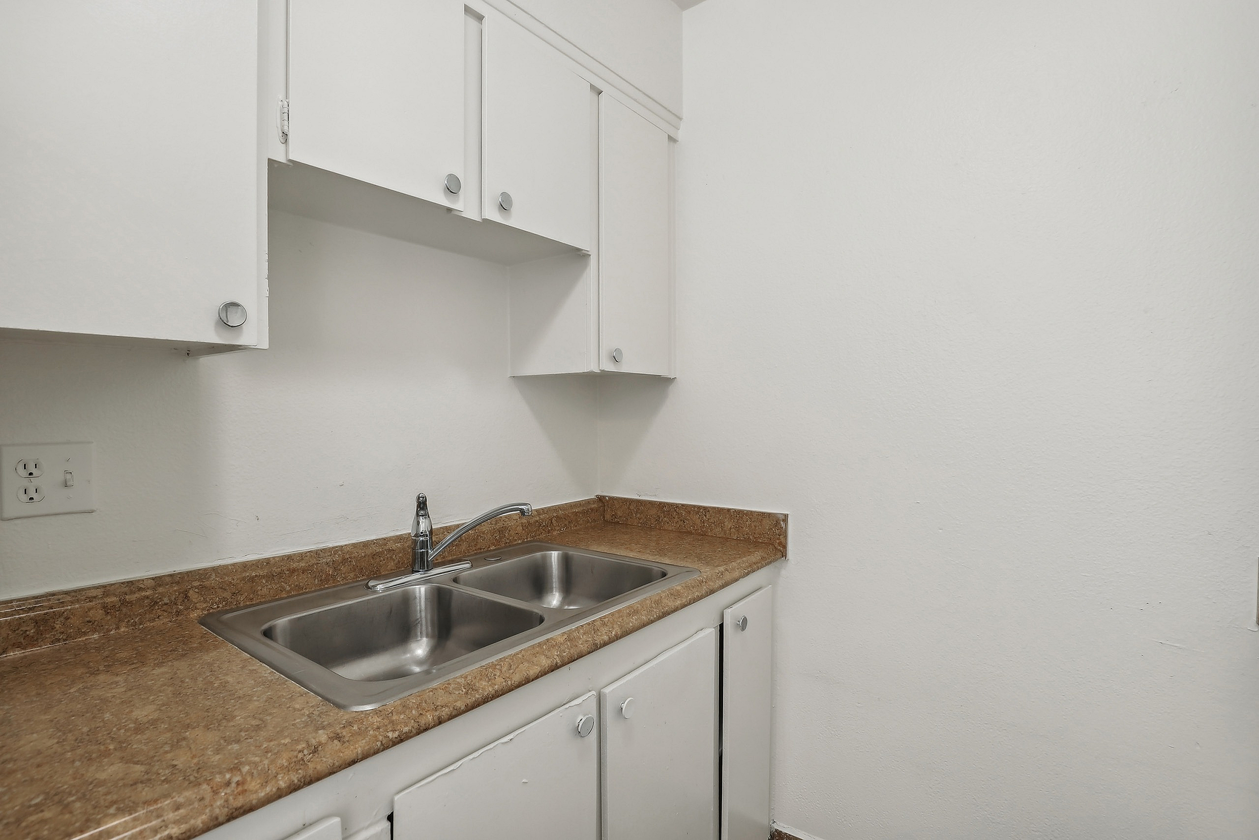 Modern kitchen with sleek countertops and stainless steel double sink, complemented by bright white cabinetry for a fresh and clean look.