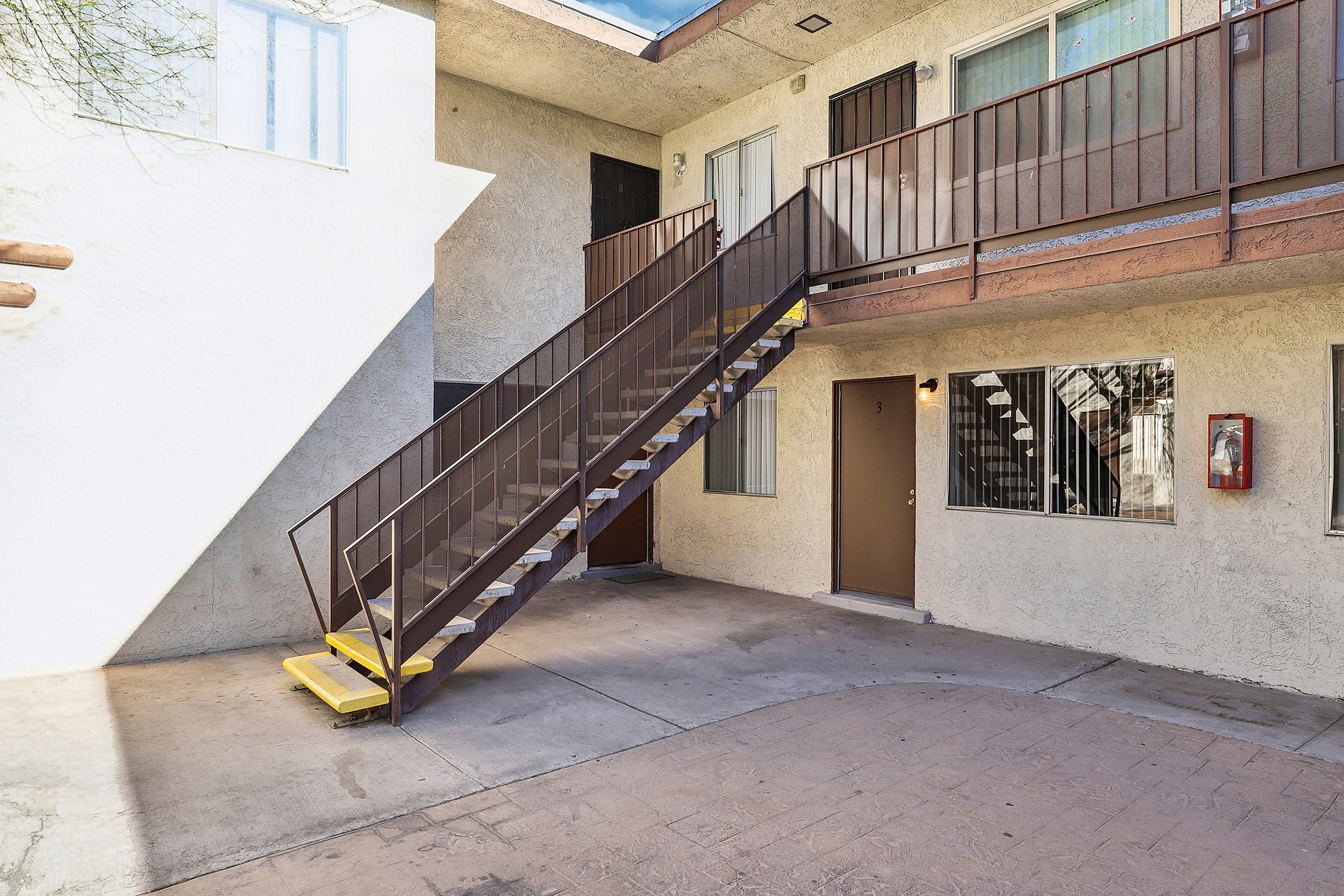 Inviting apartment exterior featuring a bright courtyard, elegant stairs, and charming second-floor balcony.