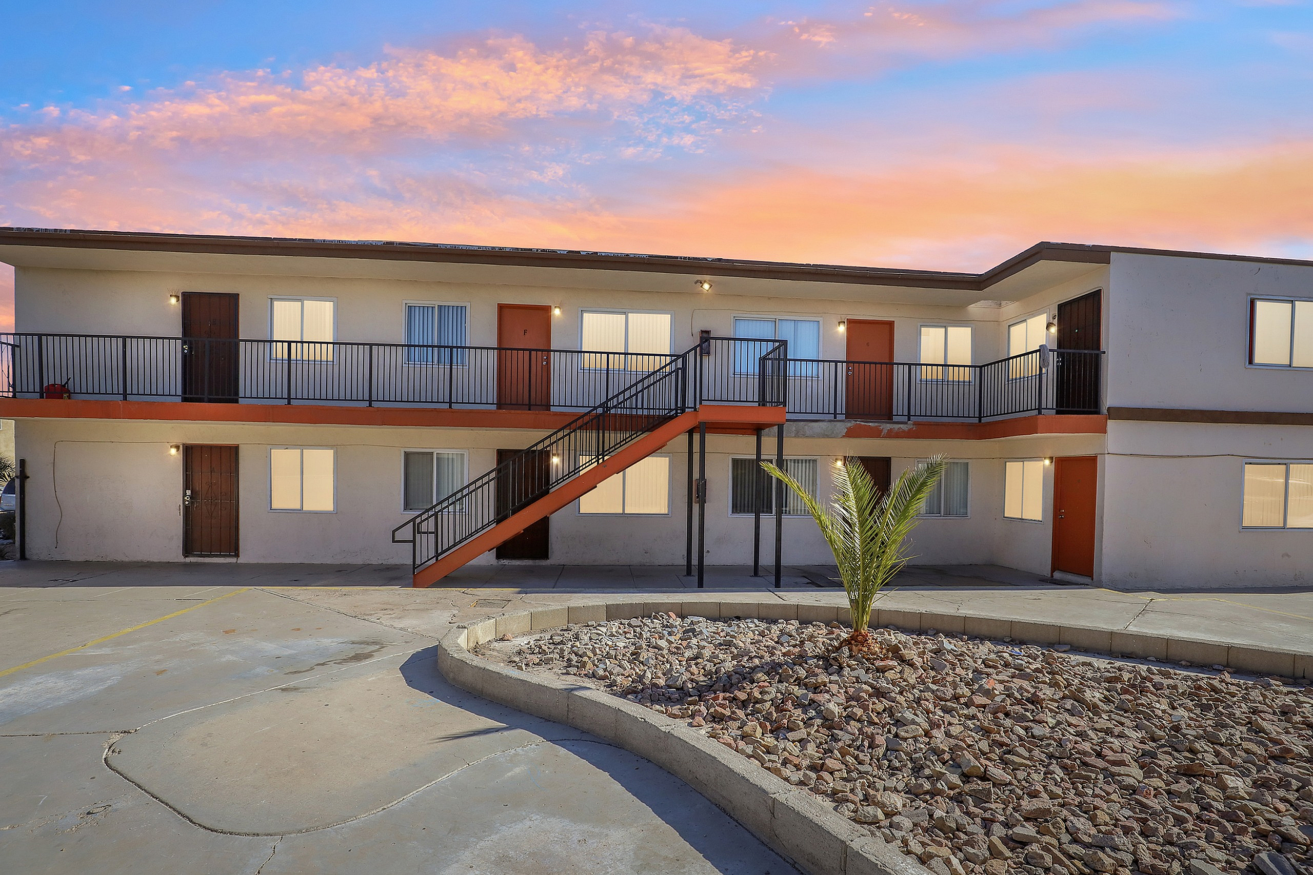 Charming apartment building with warm lighting and sunset skies, featuring distinct orange-accented entrances and a modern exterior.