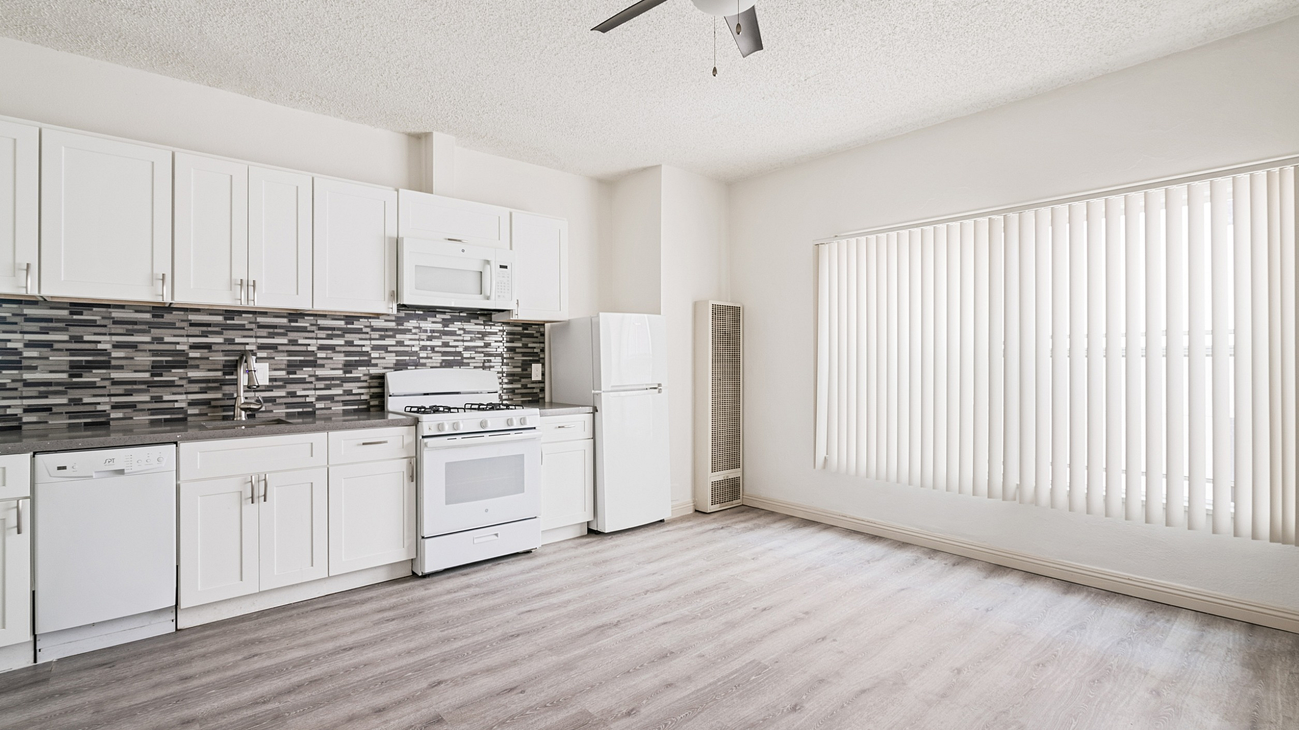 Bright modern kitchen with sleek white cabinets, stylish backsplash, and contemporary appliances, featuring large windows and elegant flooring.