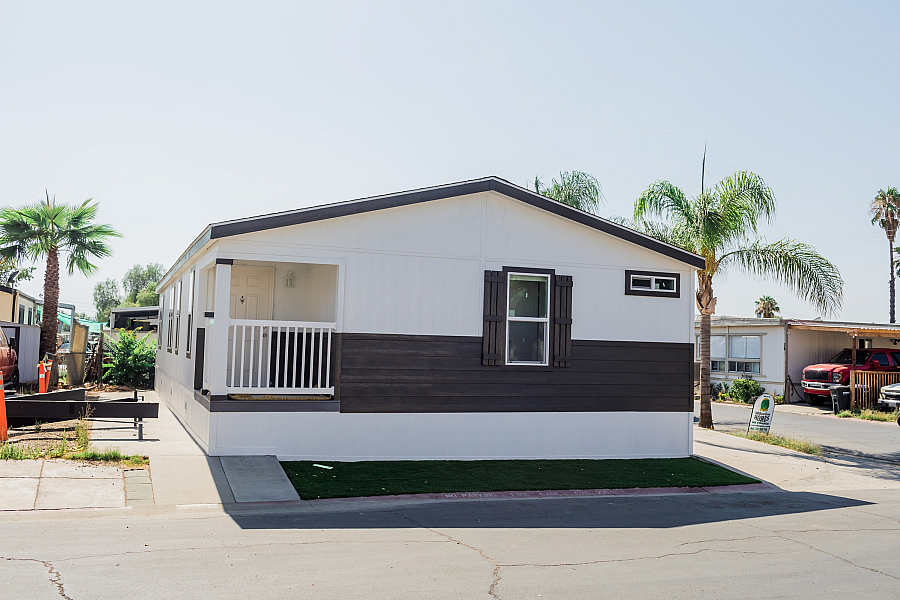 Modern manufactured home with elegant exterior, featuring a cozy porch and set against a backdrop of palm trees for a serene ambiance.