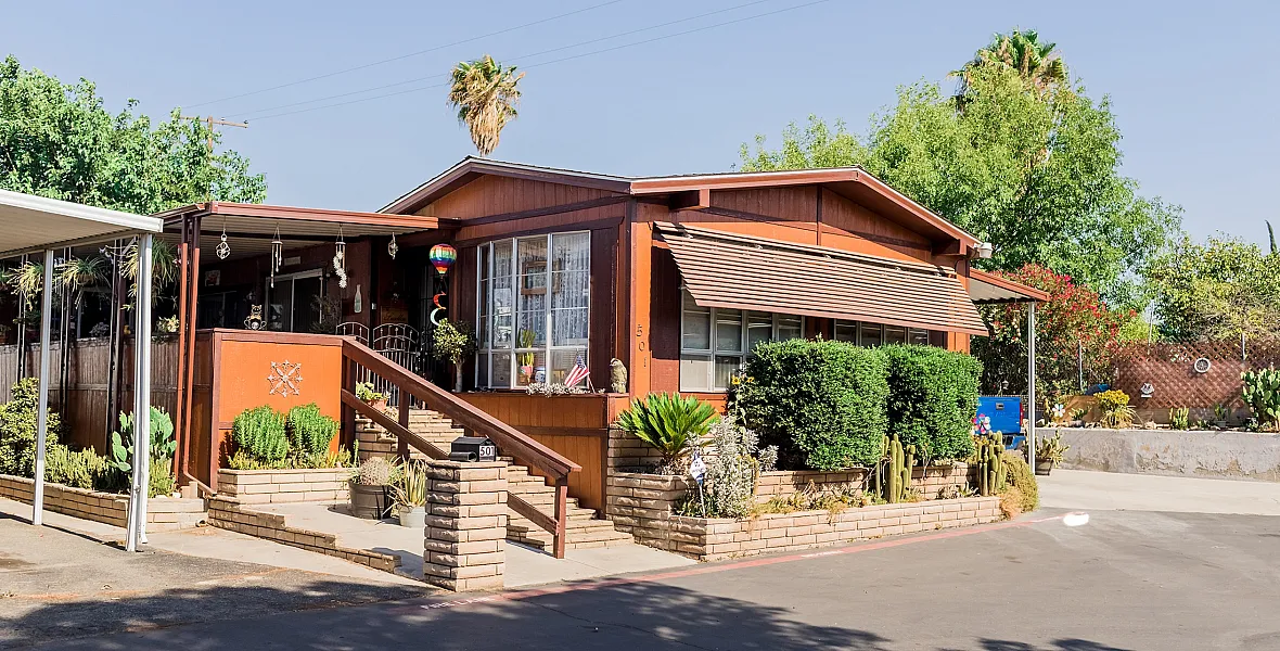 Charming rustic home with a welcoming front porch, surrounded by lush greenery and vibrant cacti in a serene neighborhood.