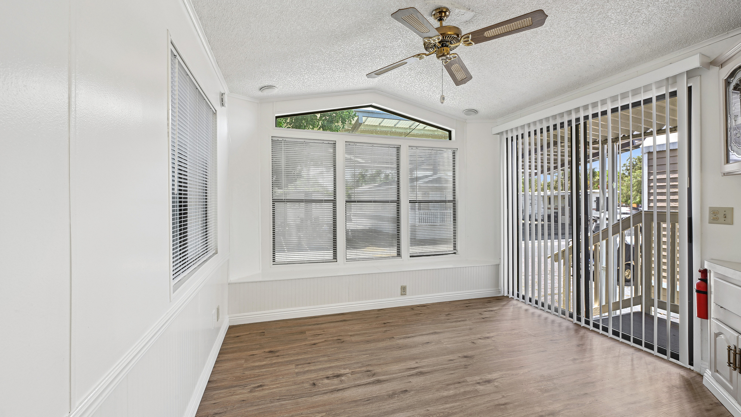 Sunlit room with elegant wood flooring, large windows, and sliding glass doors opening to a serene outdoor view.