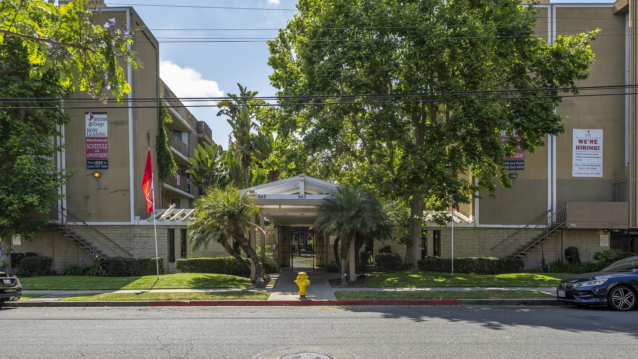 Charming apartment building with lush green landscaping and modern architecture, featuring balconies and inviting entryway.