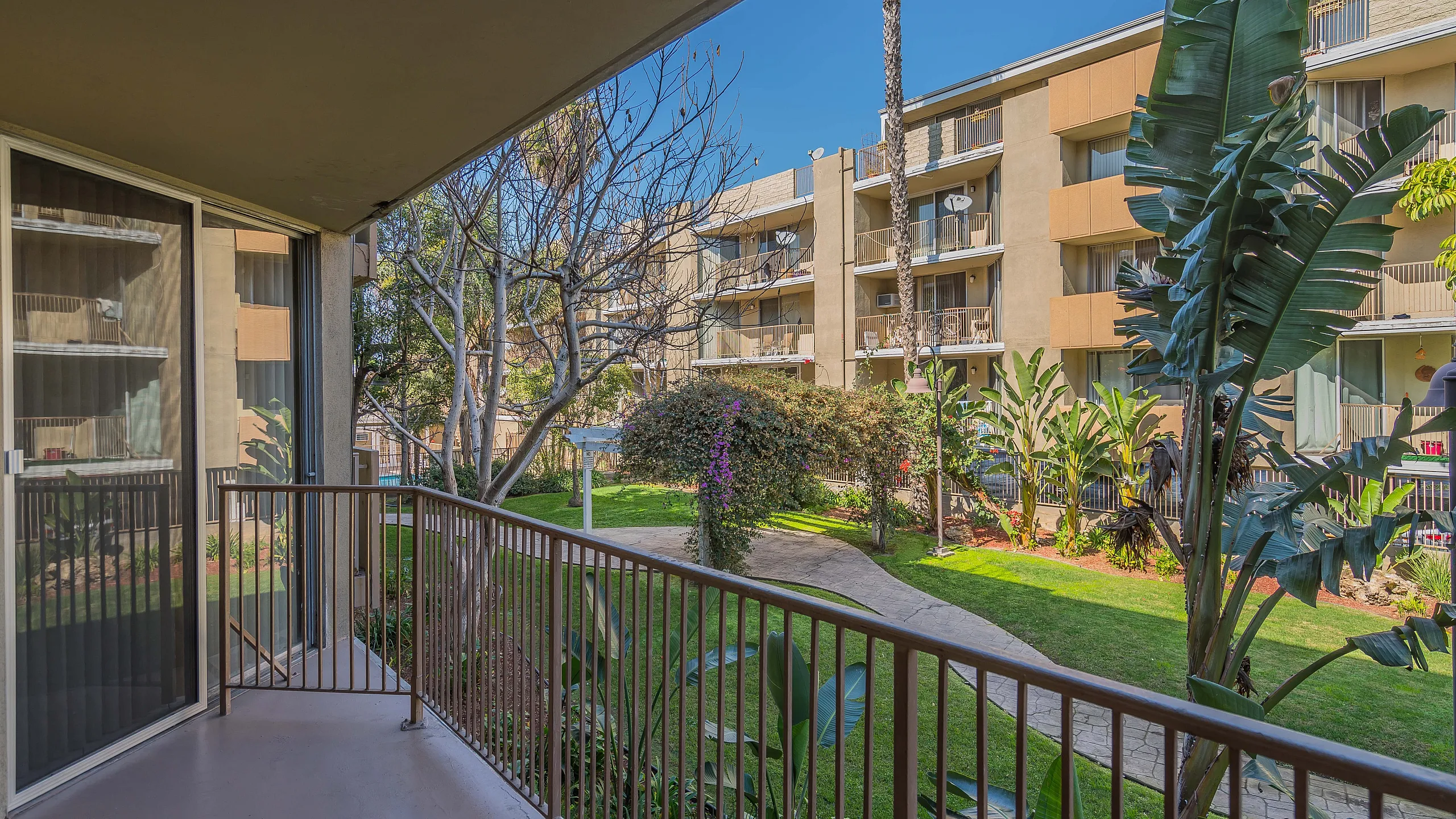 Charming balcony view overlooking lush garden and modern apartment complex, perfect for relaxation in sunny weather.