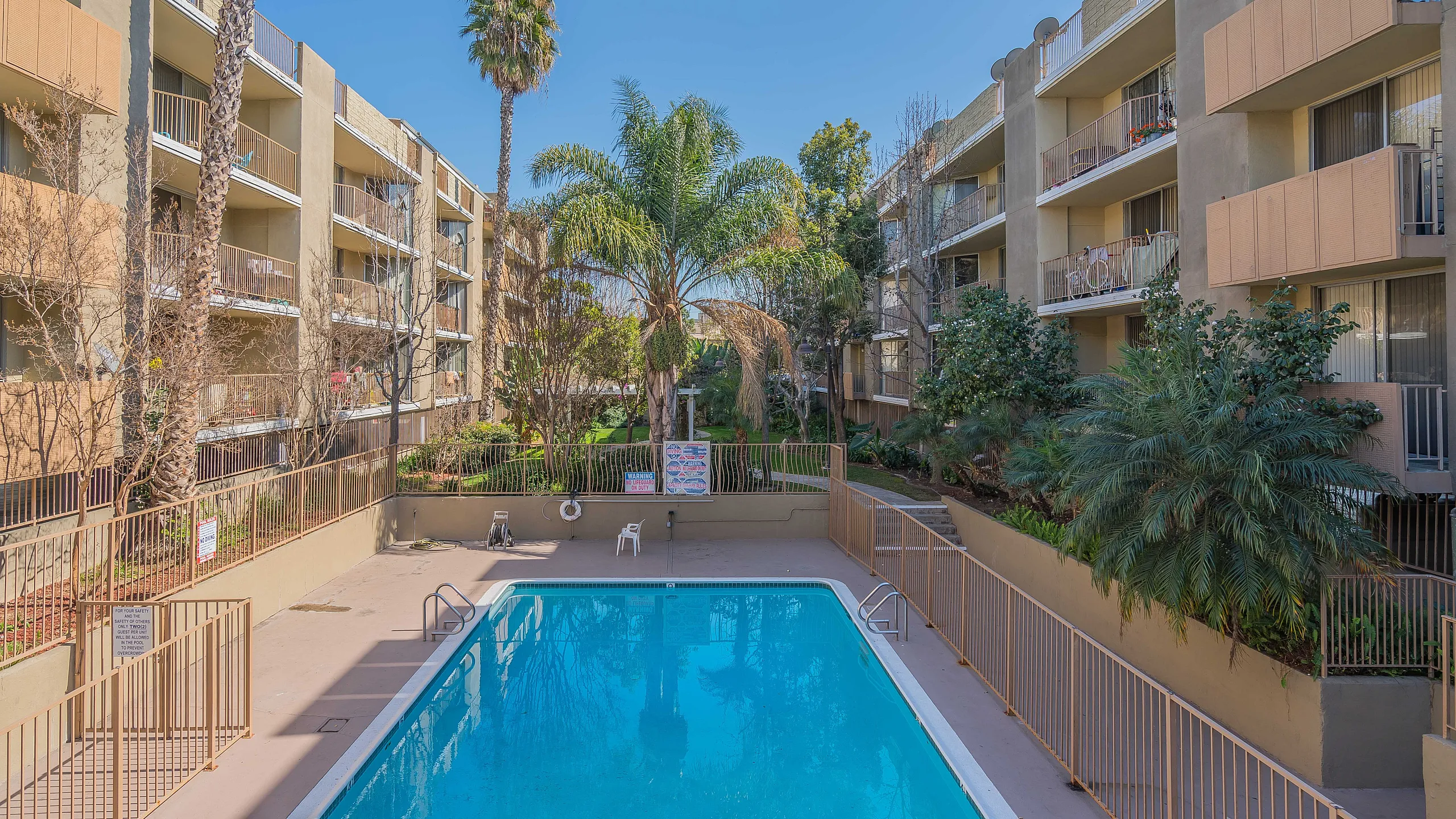 Elegant apartment complex featuring lush greenery and a sparkling swimming pool, perfect for relaxation in a sunny courtyard setting.