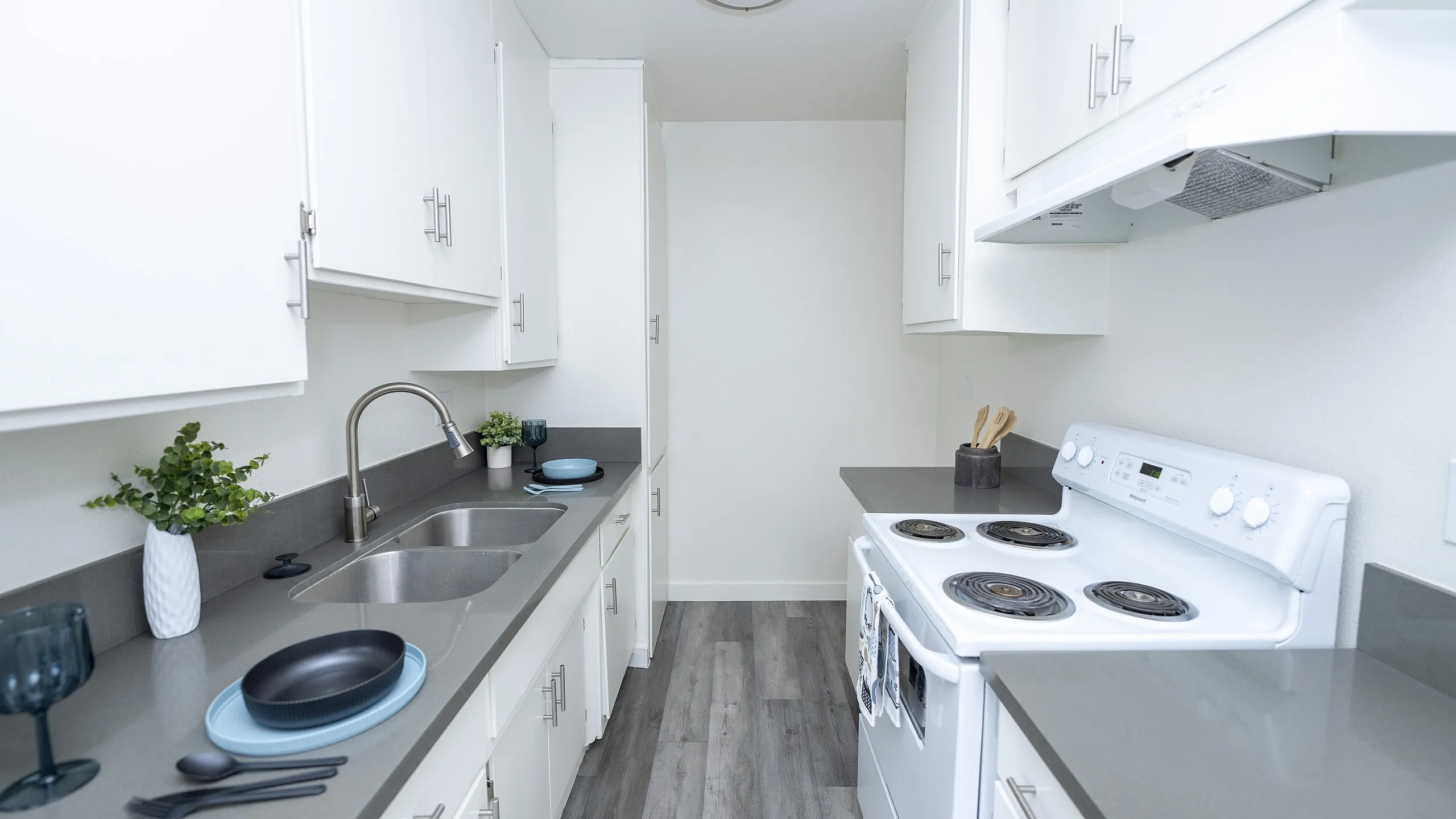 Sleek modern kitchen with white cabinetry, stainless steel sink, and elegant grey countertops.