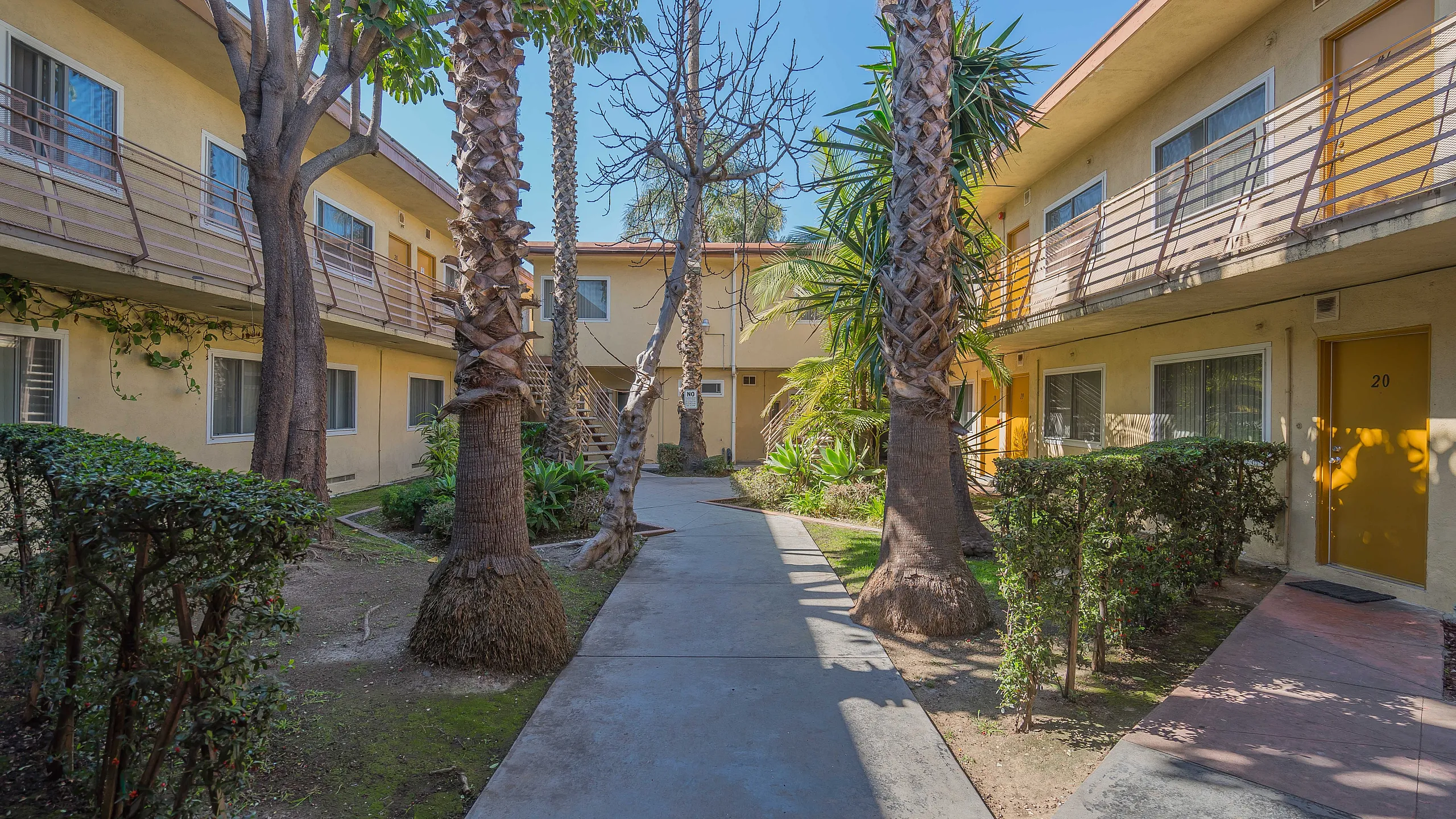 Charming apartment complex with vibrant yellow facades, surrounded by lush palm trees and greenery, offering a serene courtyard view.
