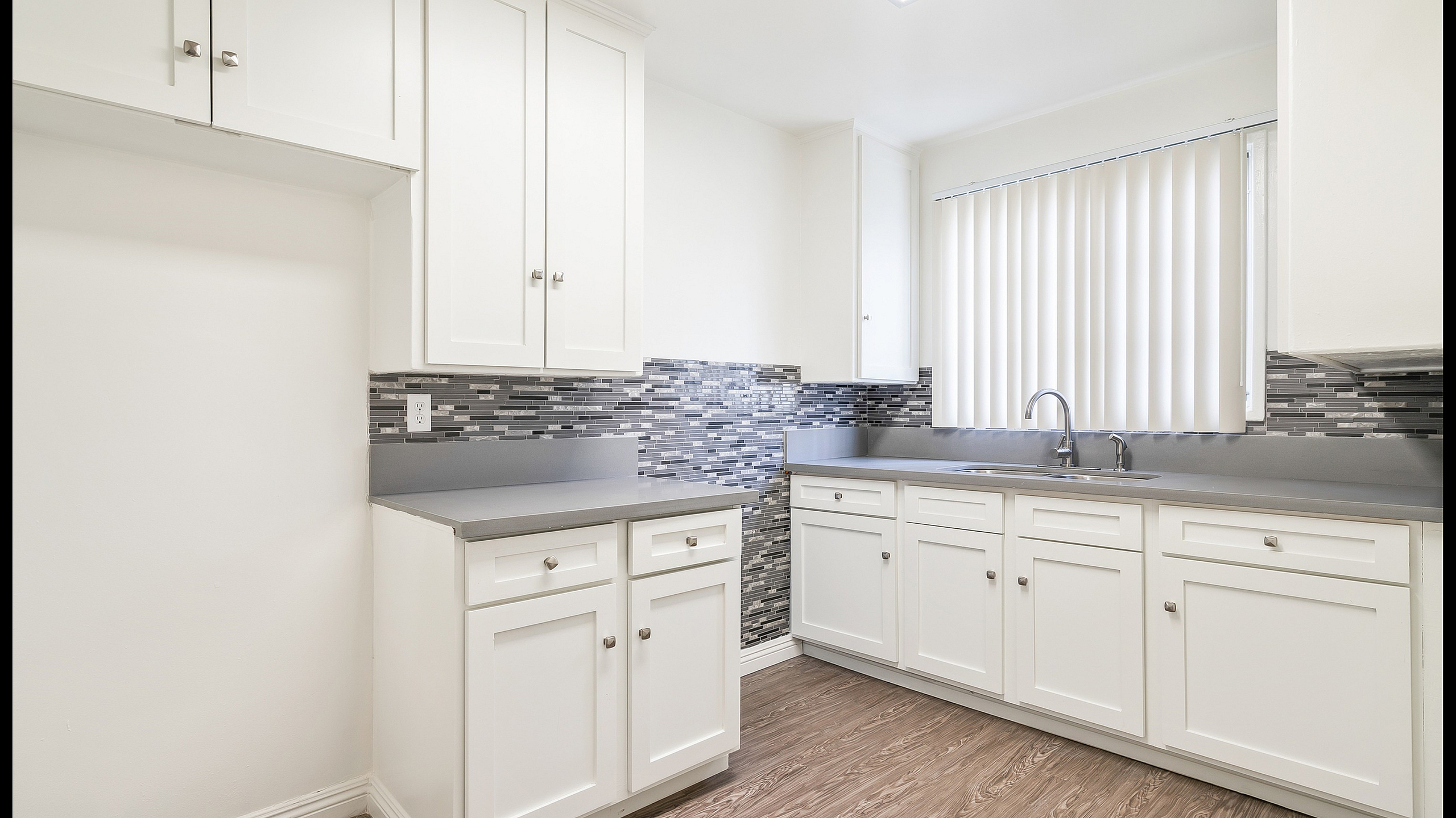 Bright, modern kitchen featuring sleek white cabinetry, elegant gray countertops, and a chic mosaic backsplash.