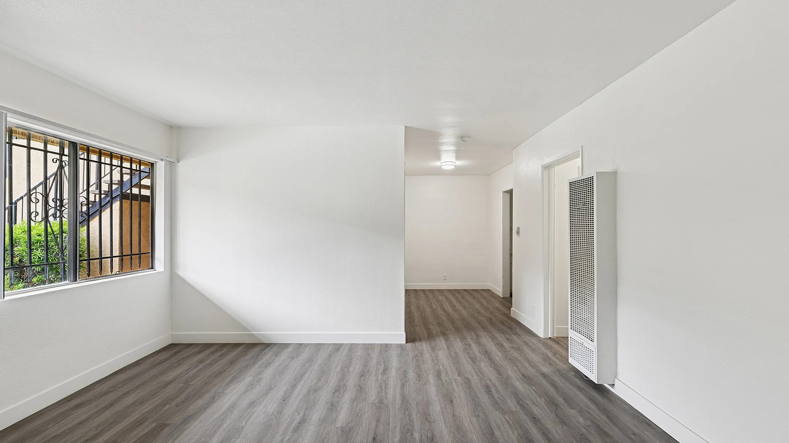 Bright and spacious room with sleek hardwood flooring, large window, and modern design elements.