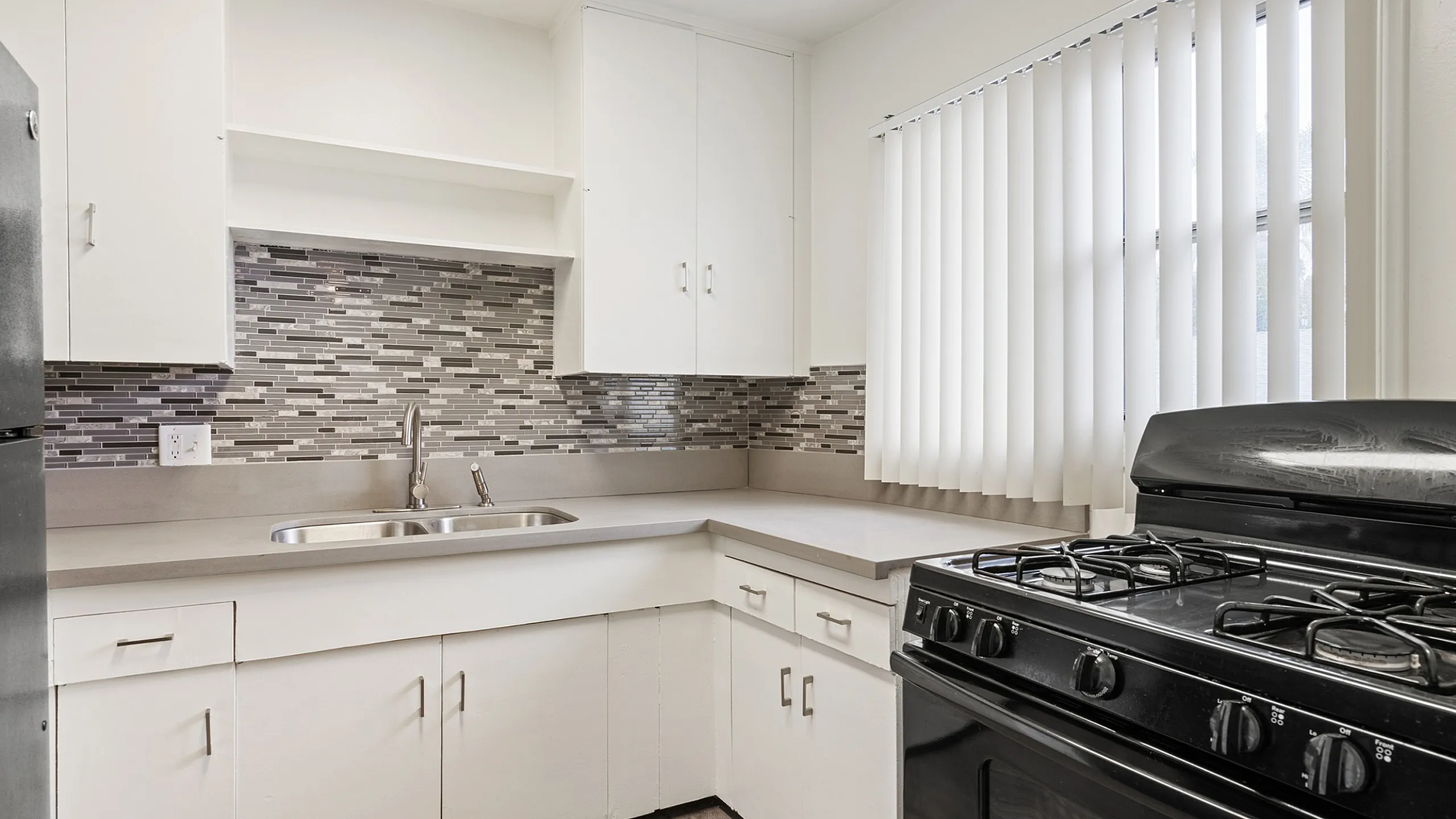 Modern kitchen with sleek black stove, stylish grey backsplash, and ample white cabinetry for a chic, functional design.