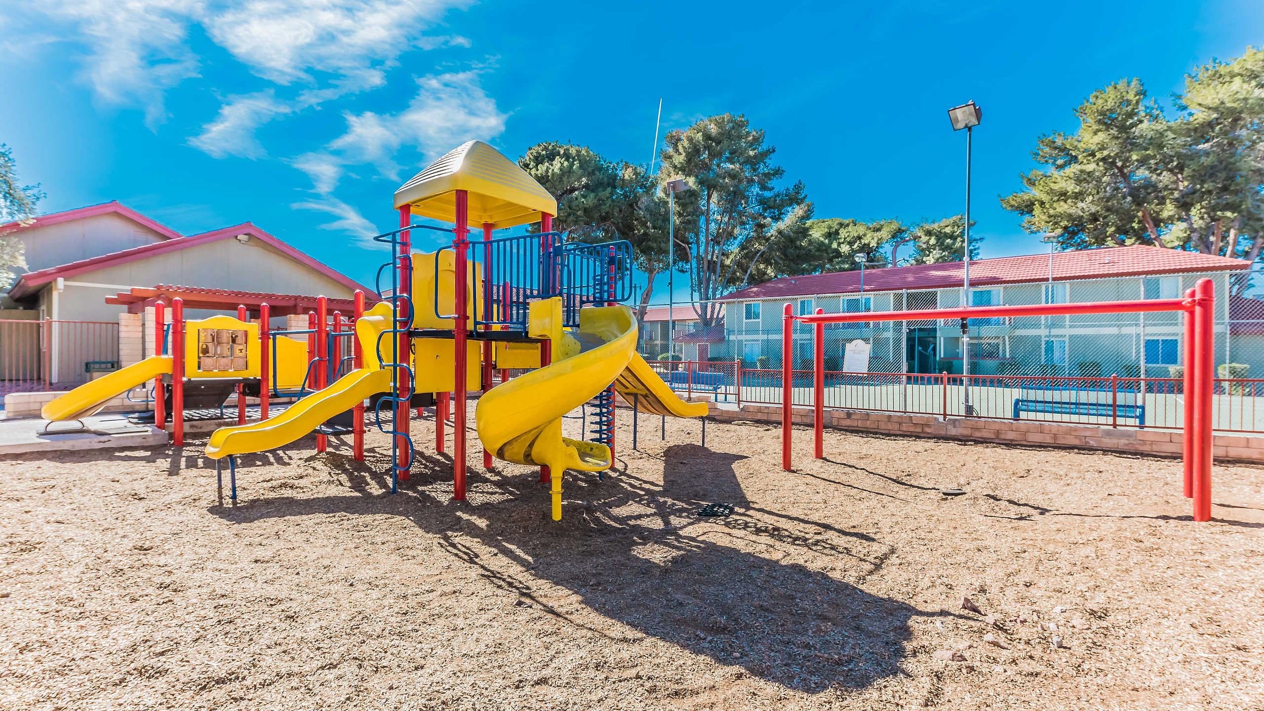 Vibrant outdoor playground featuring yellow slides and swings, surrounded by lush trees under a sunny blue sky, perfect for family fun.