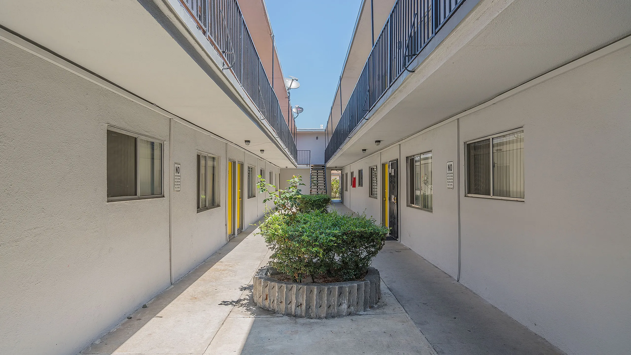 Inviting apartment complex courtyard with vibrant yellow doors and lush greenery under a clear blue sky.